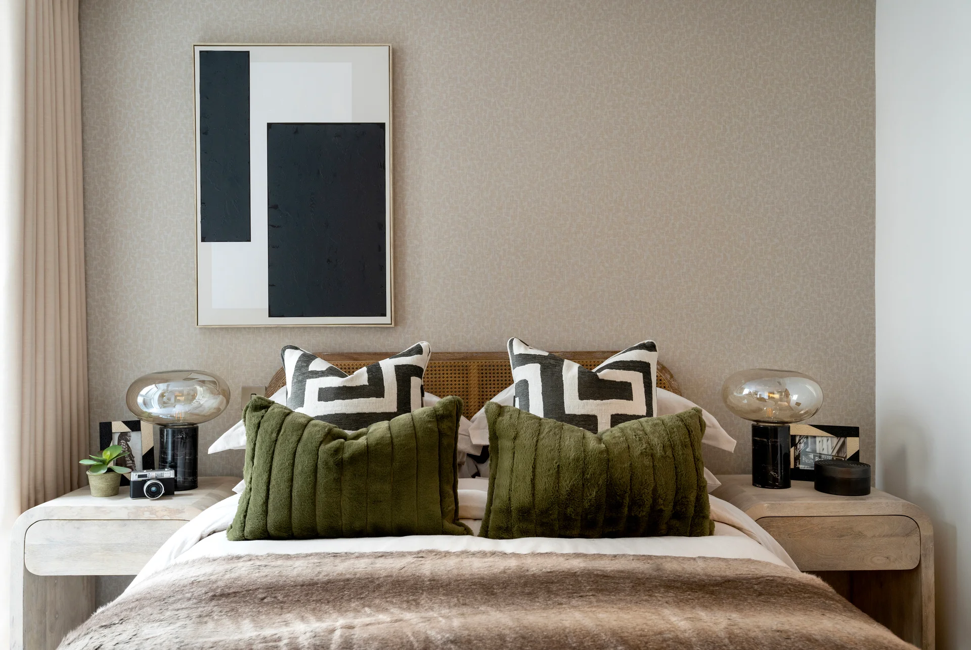 Stylish bedroom with a rattan headboard, bold monochrome cushions, olive green pillows, and matching bedside lamps and decor.