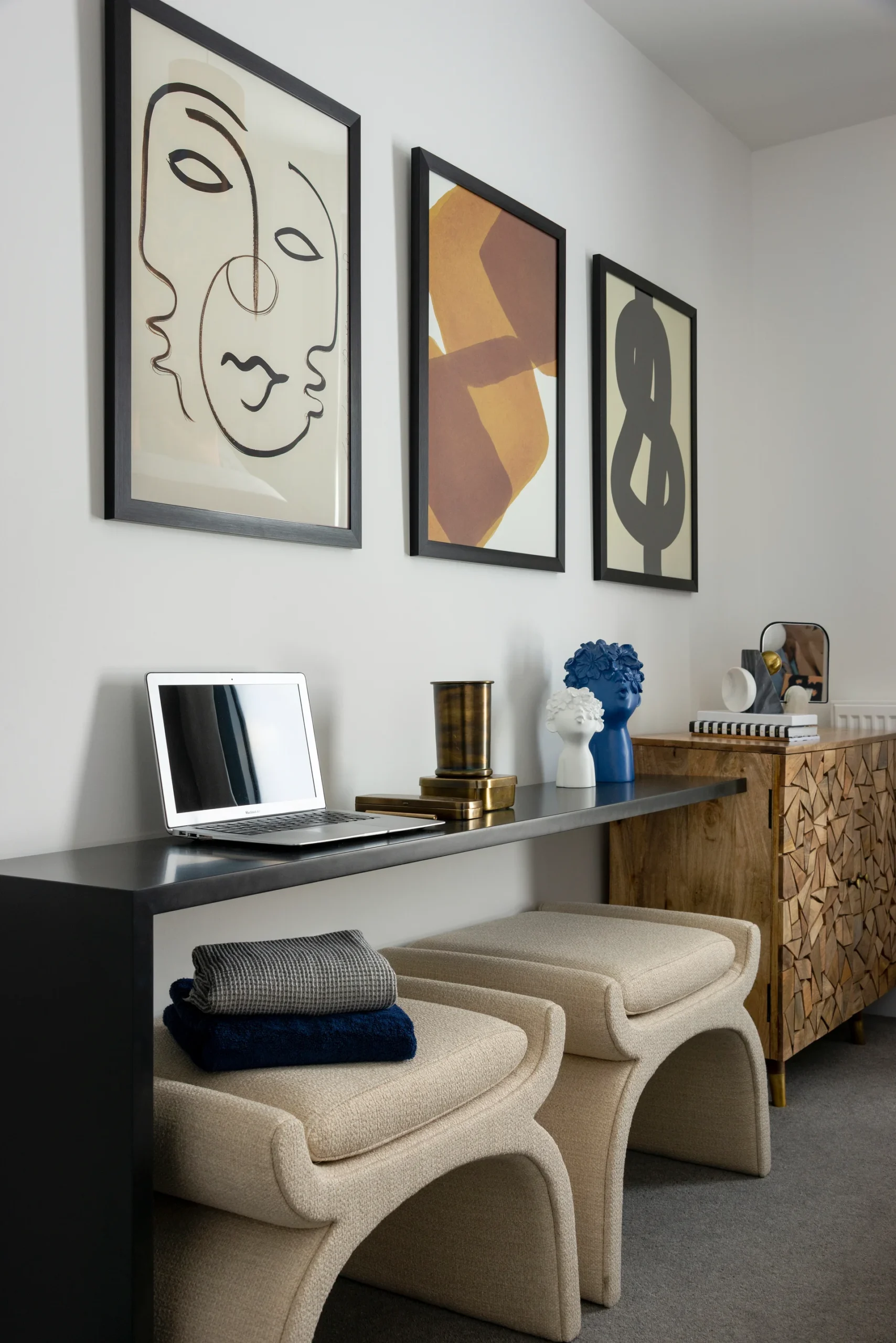 Modern interior featuring a black console table, abstract art on the walls, and two upholstered stools.