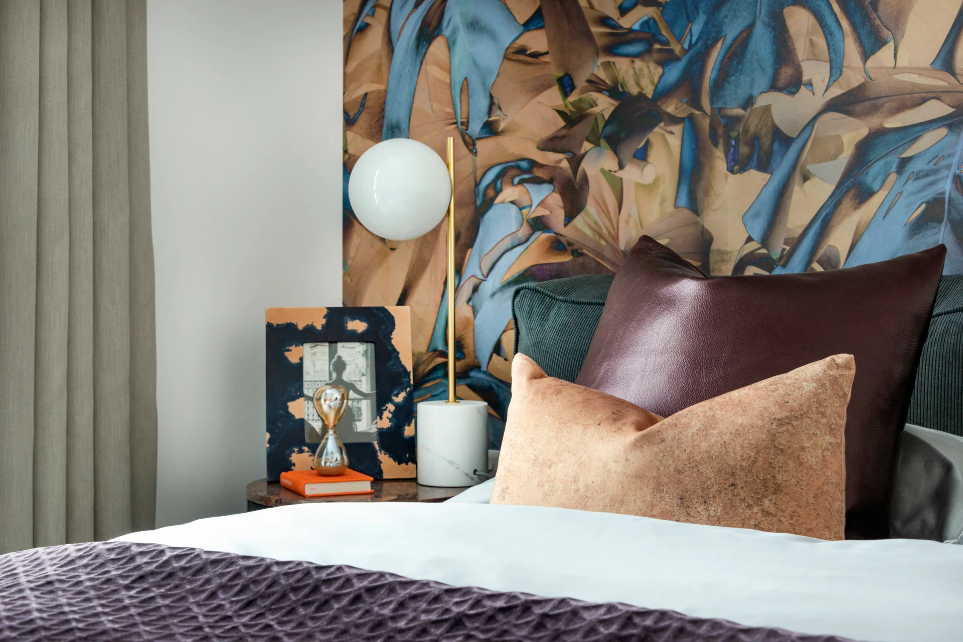 Cozy bedroom corner featuring a decorative pillow, lamp, and floral wallpaper.