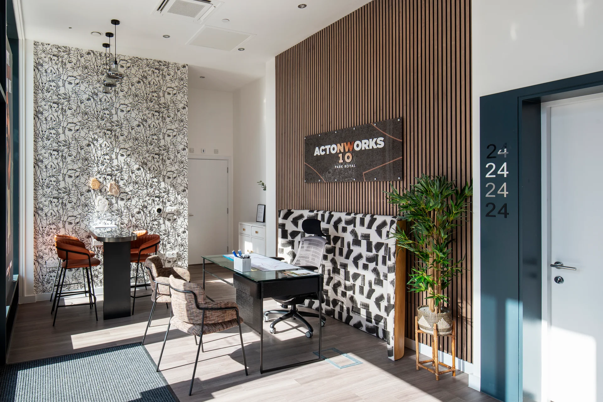 Modern office space featuring a patterned wall, desk, chairs, and decorative plants with a sign reading "ACTION WORKS 10.
