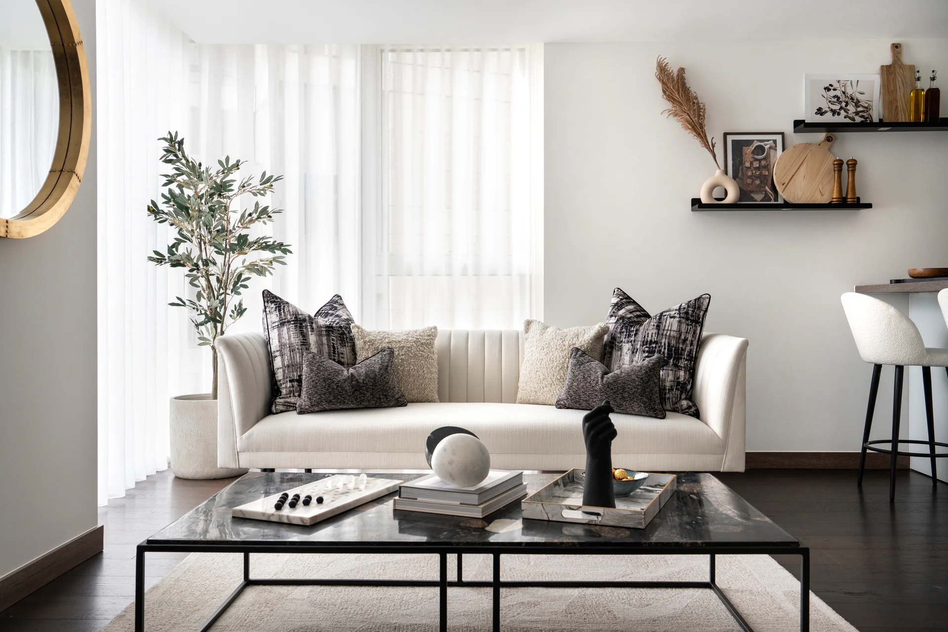 Modern living room featuring a light sofa with textured pillows, a coffee table, and a decorative plant beside a window.