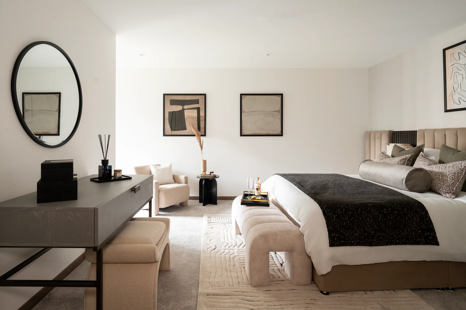 Modern bedroom featuring a large bed, seating area, a round mirror, and minimalist decor.