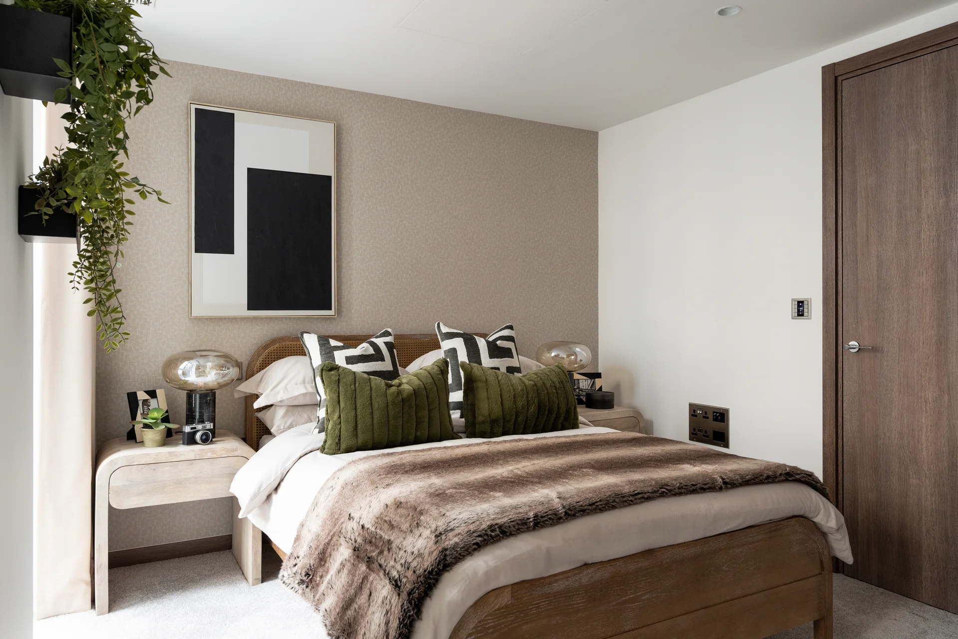 Modern bedroom featuring a bed with decorative pillows, artwork on the wall, and a plant by the window.