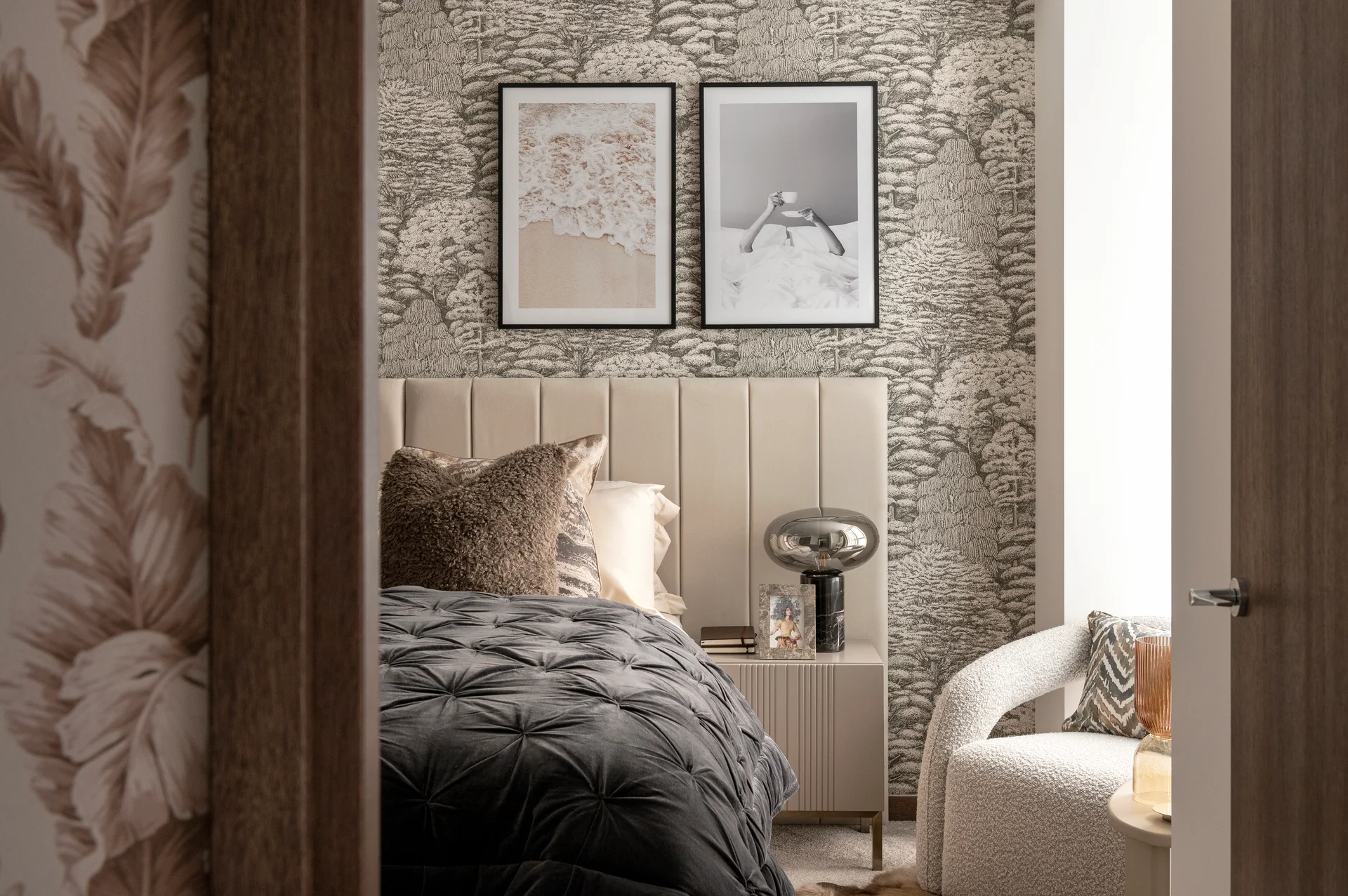 Cozy bedroom with textured wallpaper, plush bedding, framed art, and a small seating area.