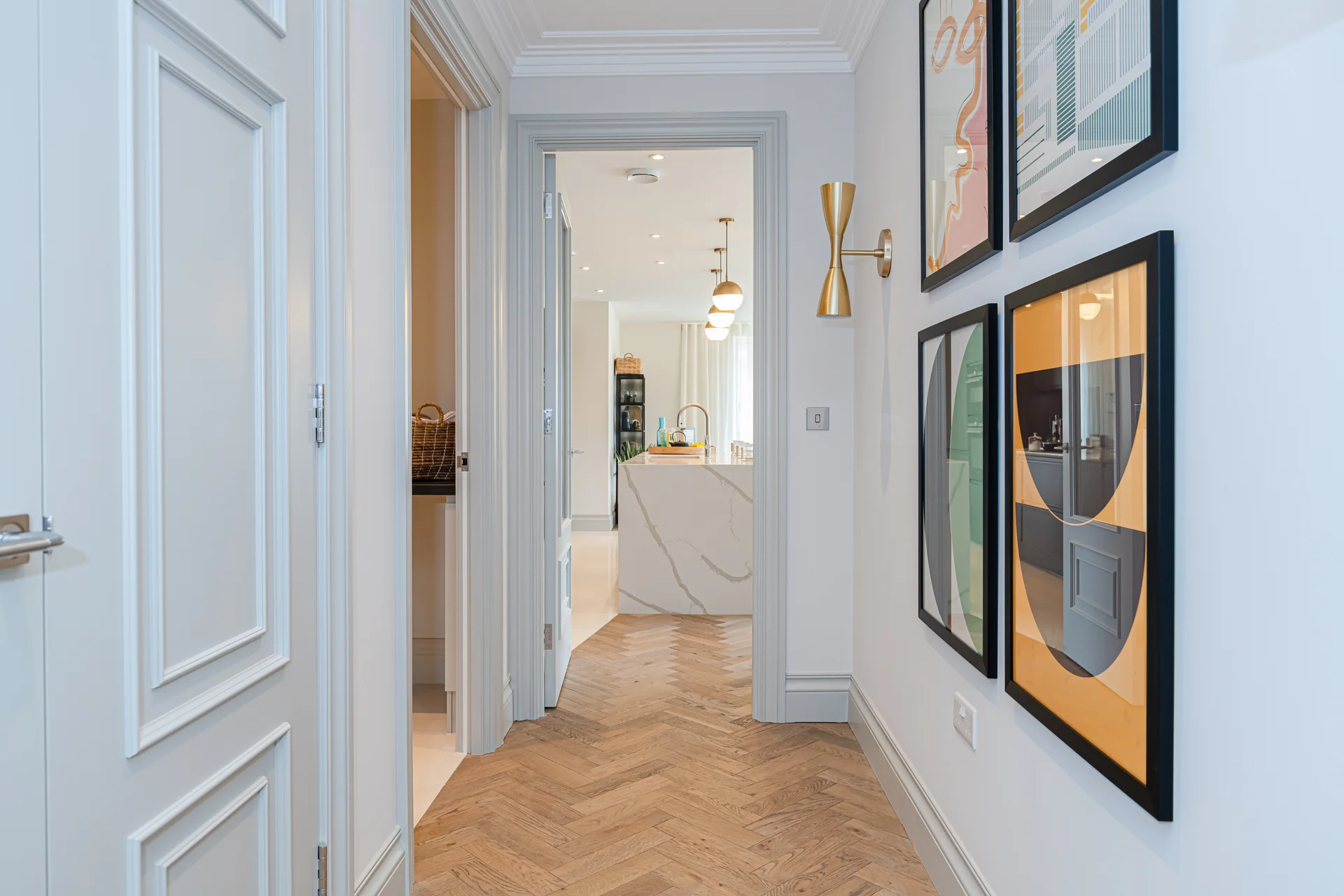 Bright hallway featuring framed artwork, herringbone flooring, and a glimpse into adjacent rooms.