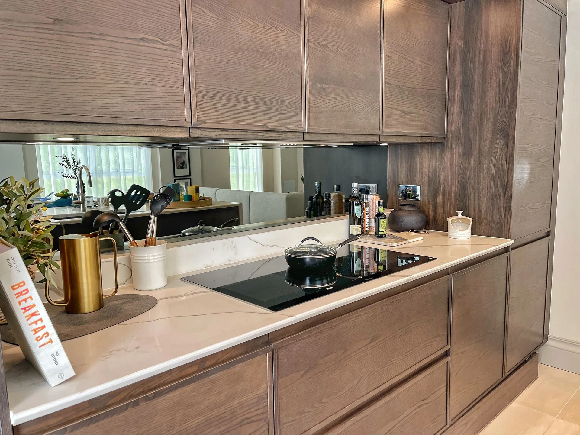 Modern kitchen featuring sleek wooden cabinetry, a stovetop, and a decorative arrangement with cooking utensils and plants.
