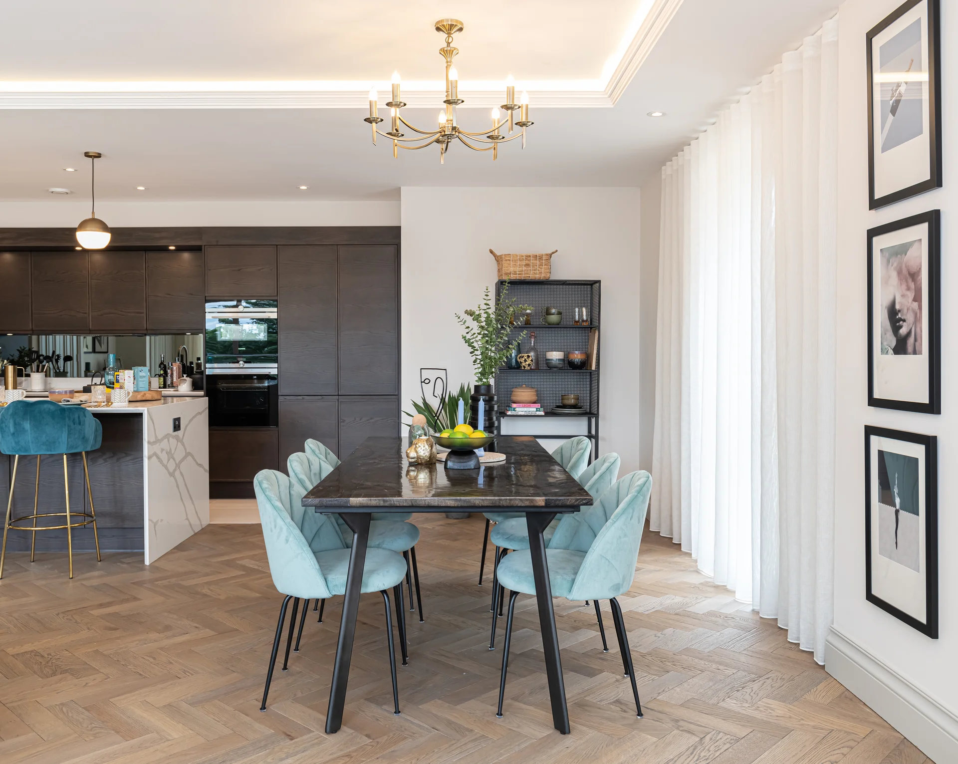 Modern dining area featuring a black table with teal chairs, a kitchen unit, and framed artwork on the walls.