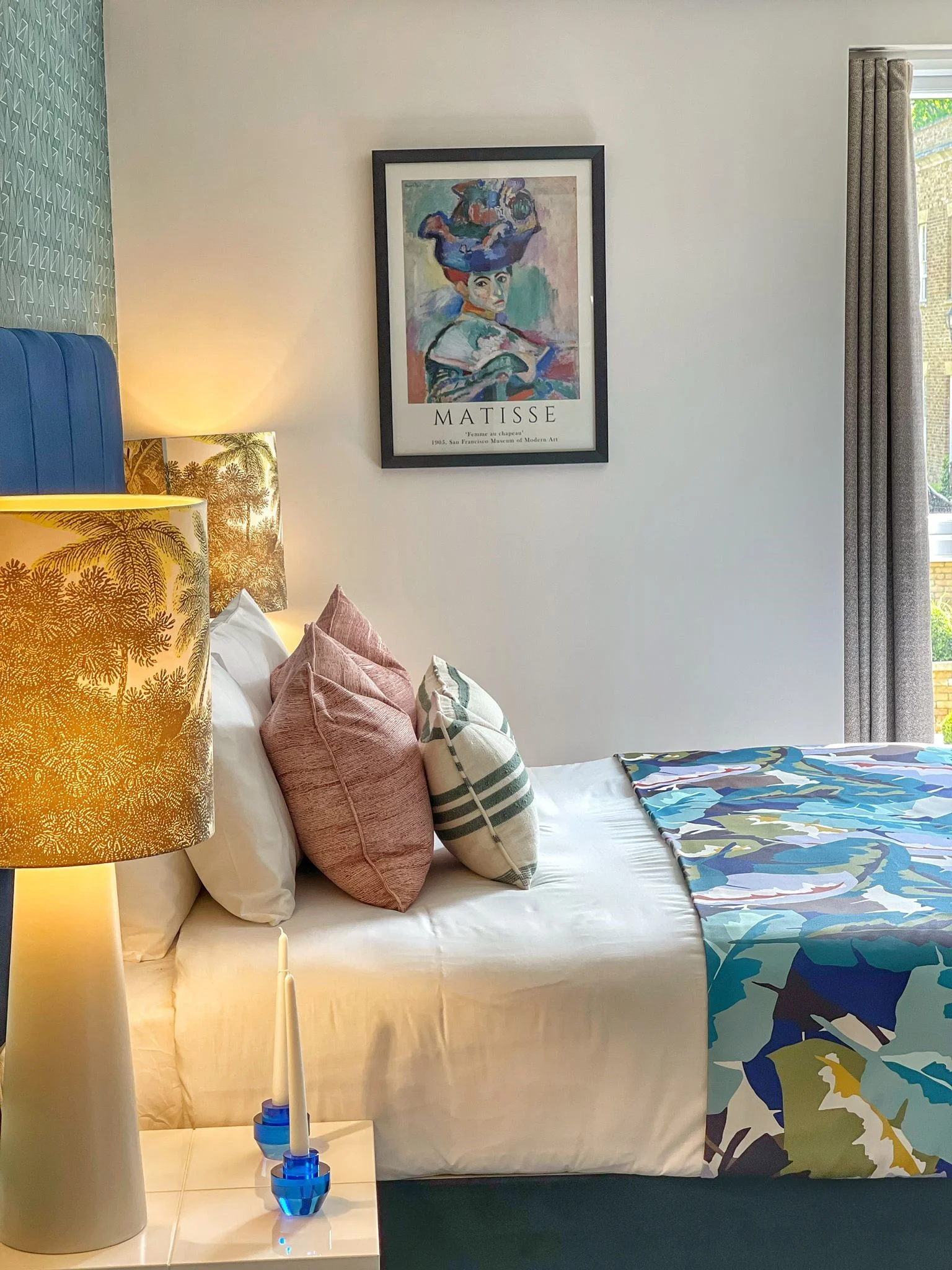Cozy bedroom with a decorated bed, colorful pillows, a patterned blanket, and framed artwork on the wall.