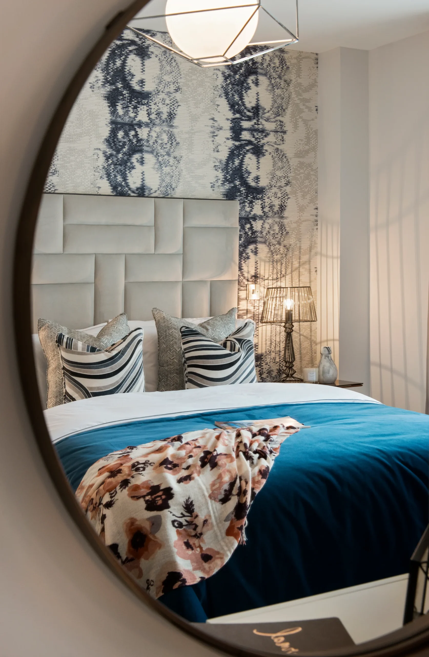 Stylish bedroom with a blue bedspread, patterned pillows, a floral throw, and modern wall decor reflected in a circular