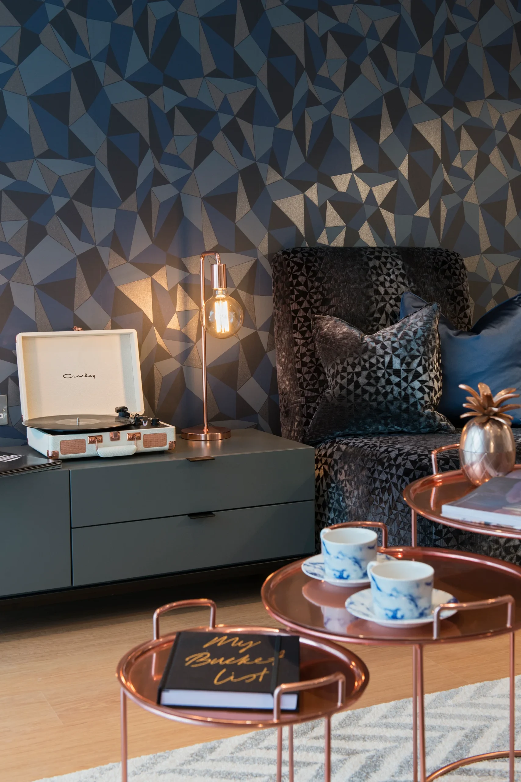 Cozy living room setting with geometric wallpaper, a record player, elegant coffee tables, and decorative pillows.