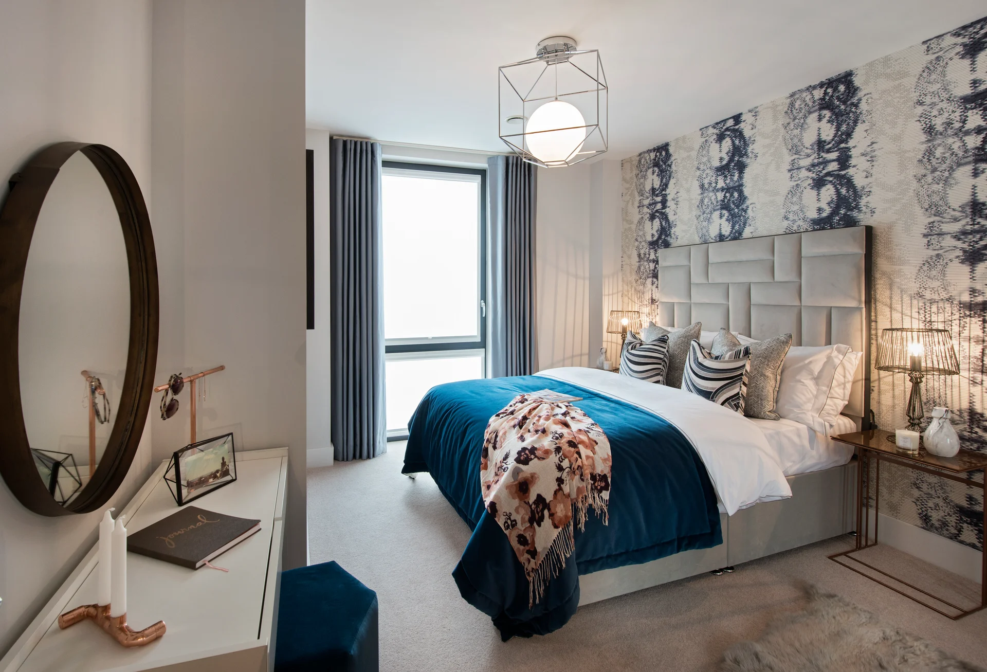 Modern bedroom featuring a large bed, decorative pillows, a stylish mirror, and patterned wallpaper.