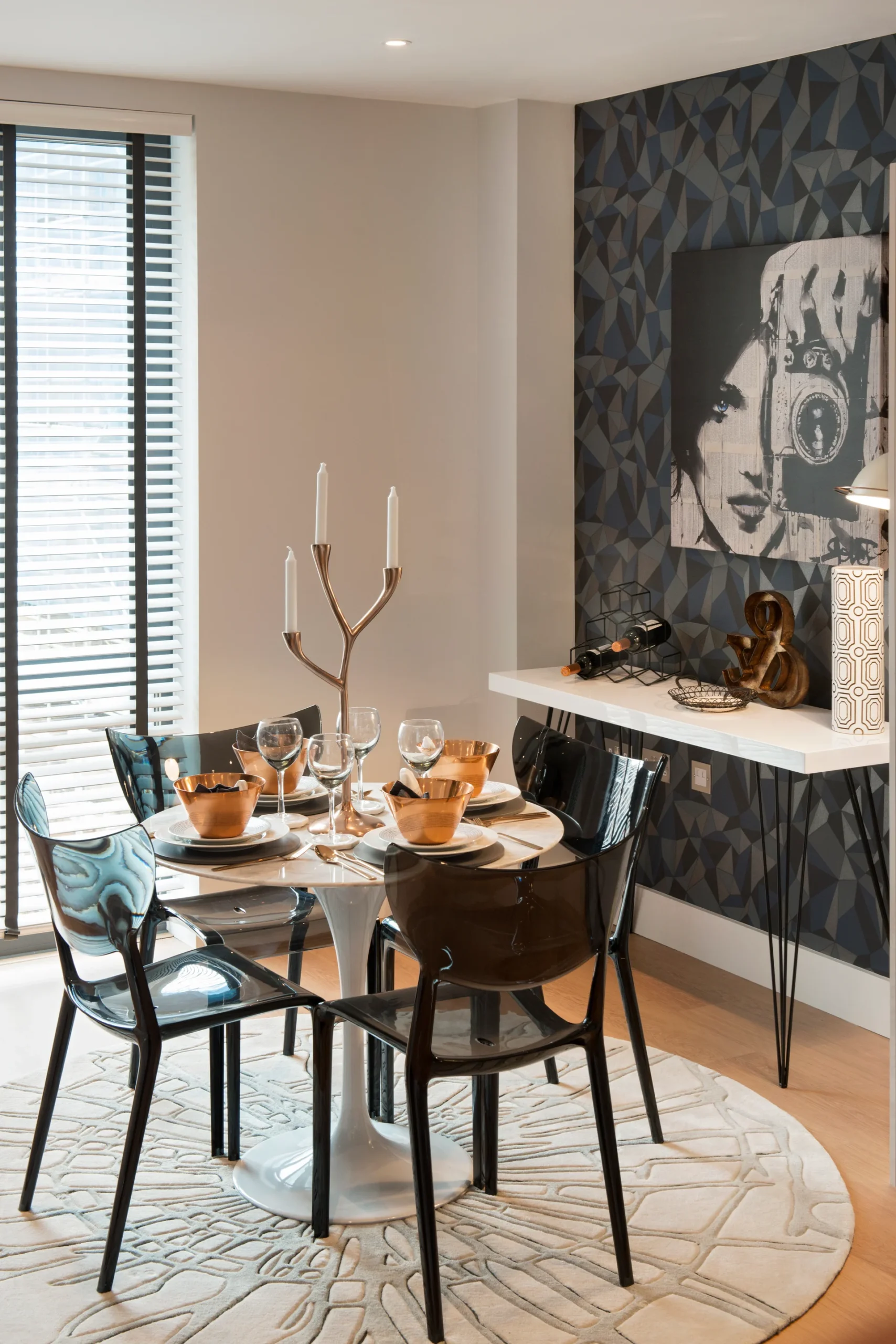 Modern dining area featuring a round table set for four, with elegant decor and an artistic wall design.