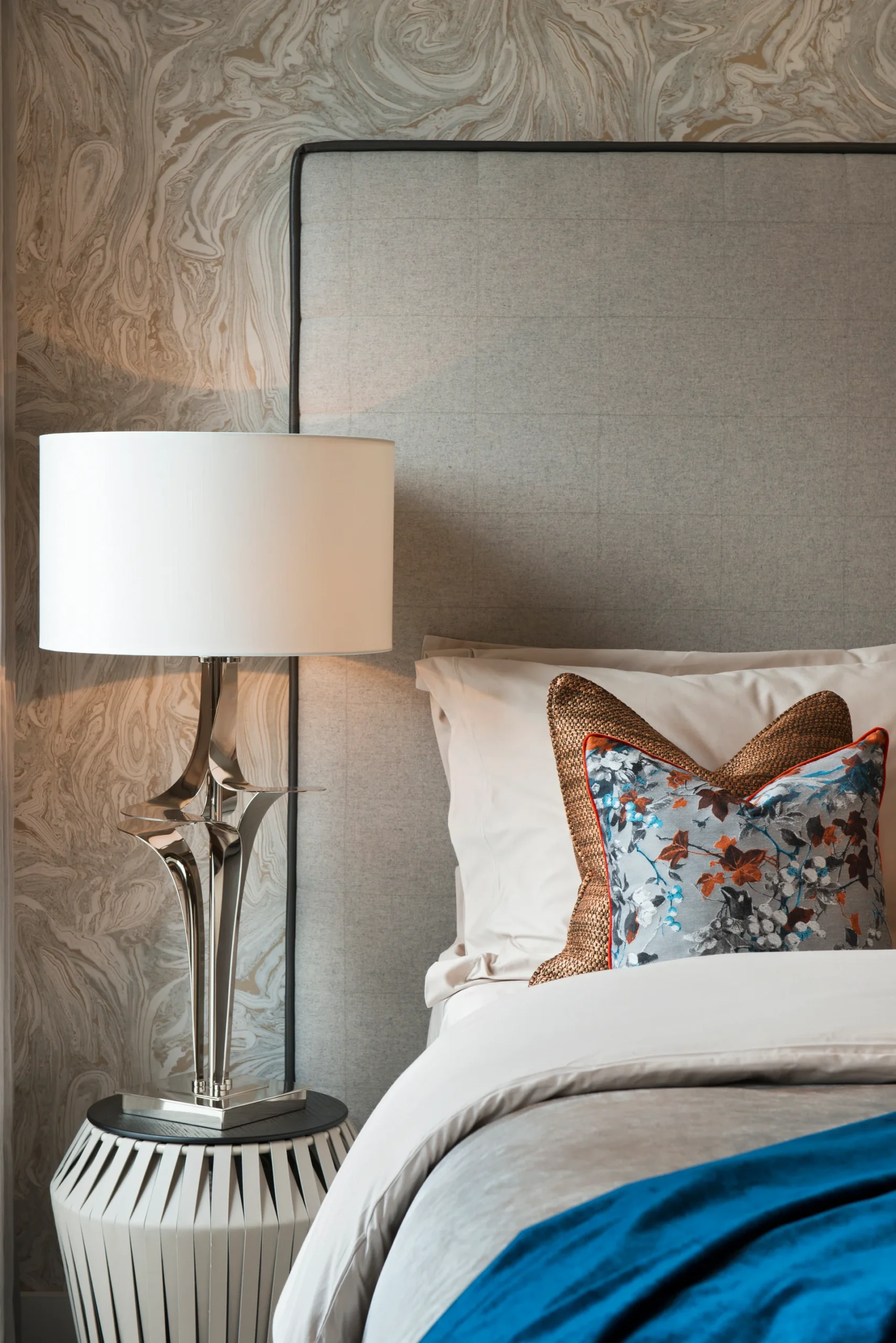 Modern bedroom featuring a gray upholstered headboard, decorative pillows, and a stylish lamp on a nightstand.