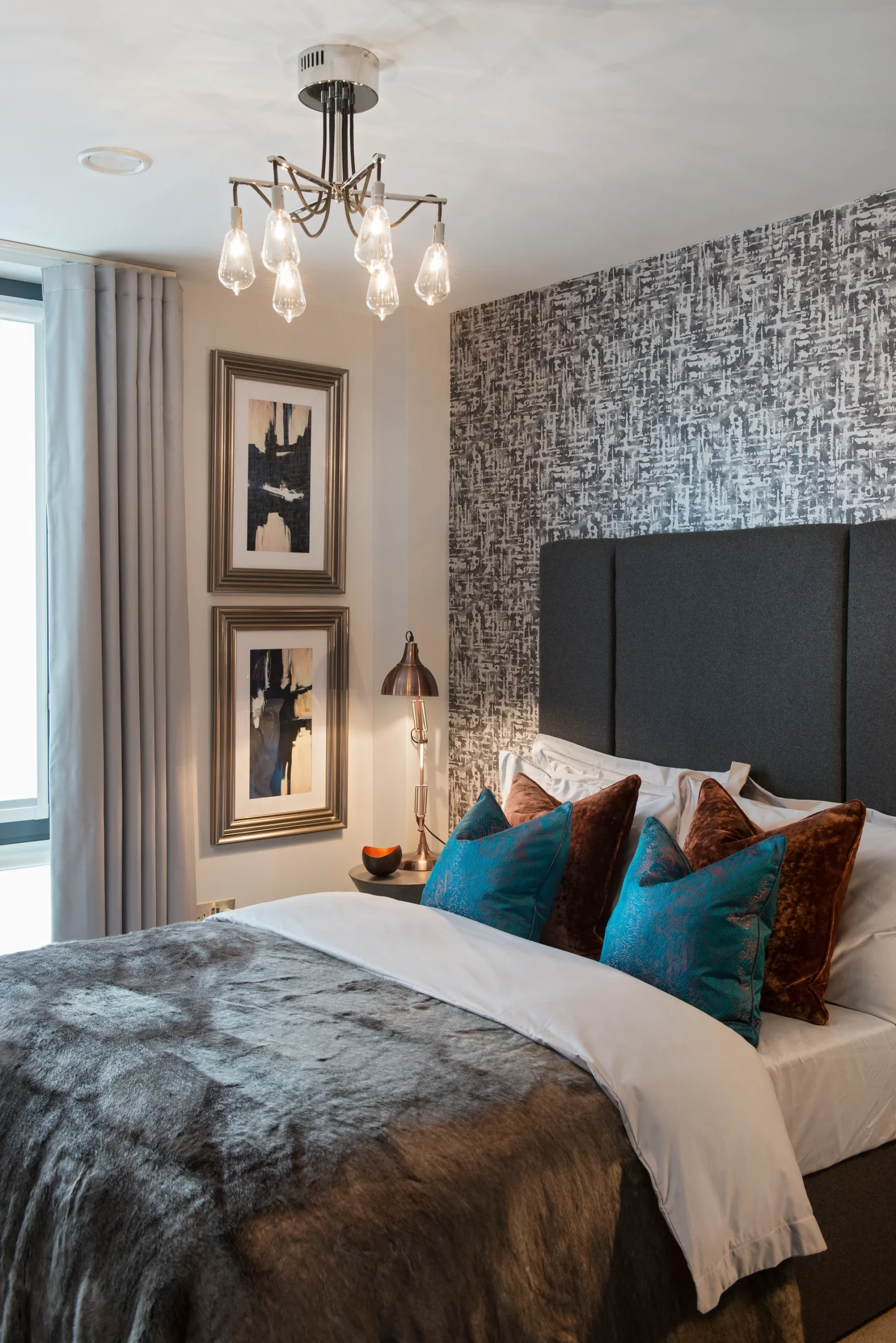 Modern bedroom featuring a stylish bed with decorative pillows, artwork on the wall, and a unique chandelier.