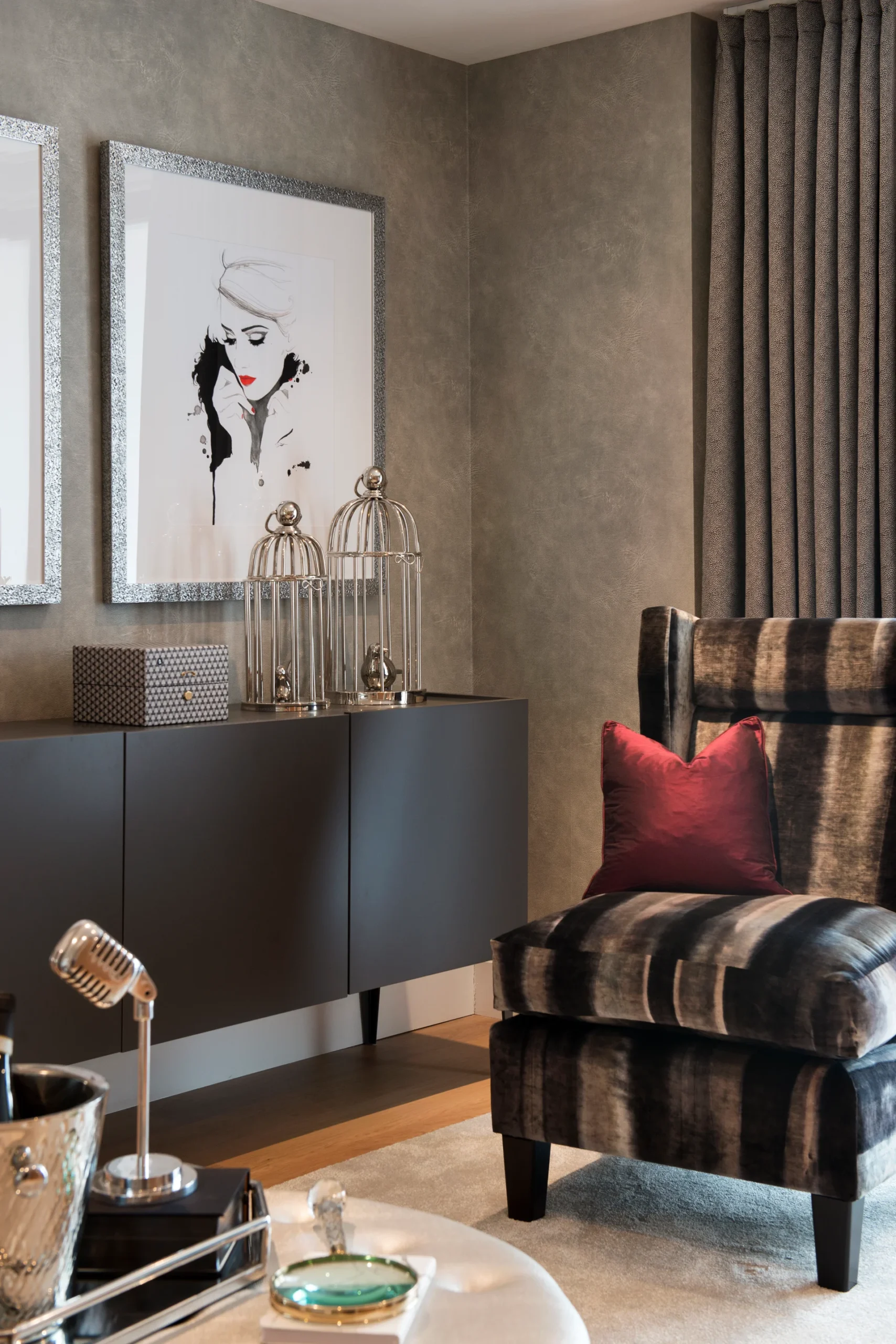 Stylish living room corner featuring a striped armchair, elegant artwork, and decorative accents on a sleek cabinet.
