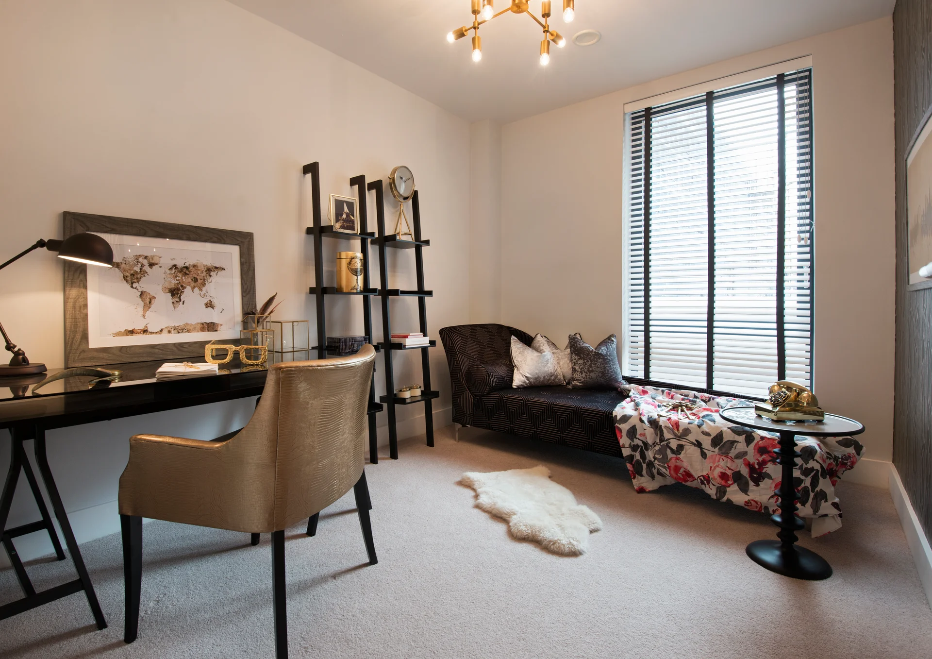 Cozy office space featuring a desk, chair, bookshelves, and a sofa with a blanket by a window with blinds.