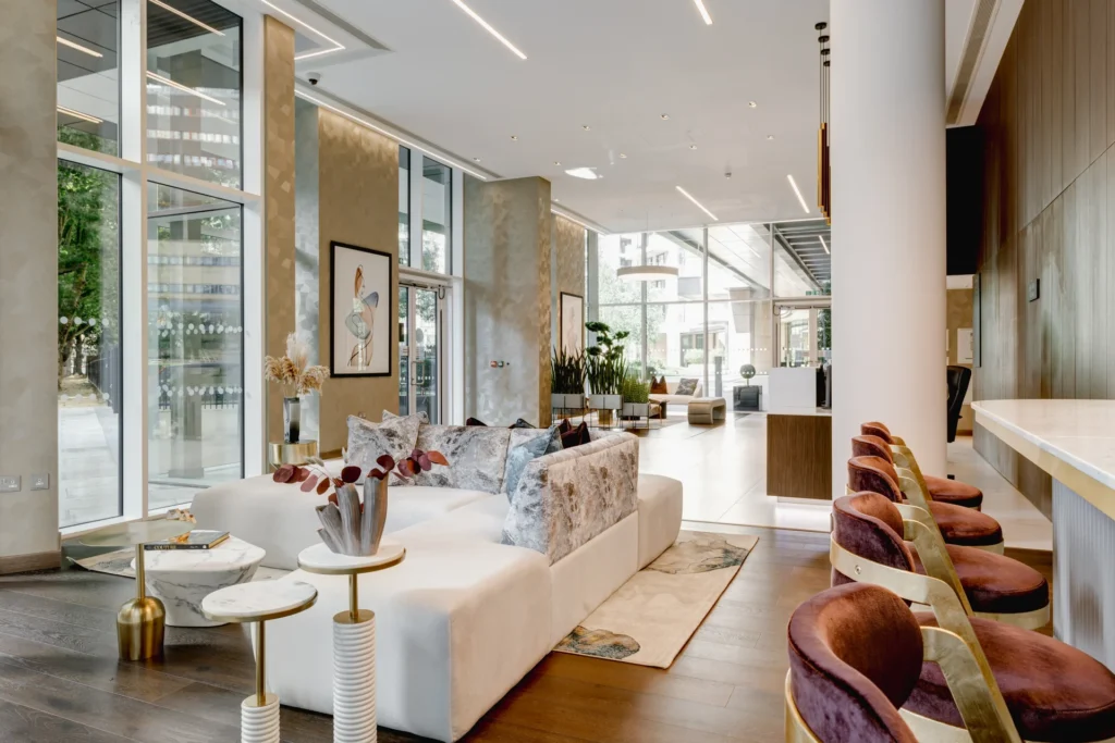 Modern reception area with a white sofa, colorful cushions, and stylish seating, featuring large windows and greenery.
