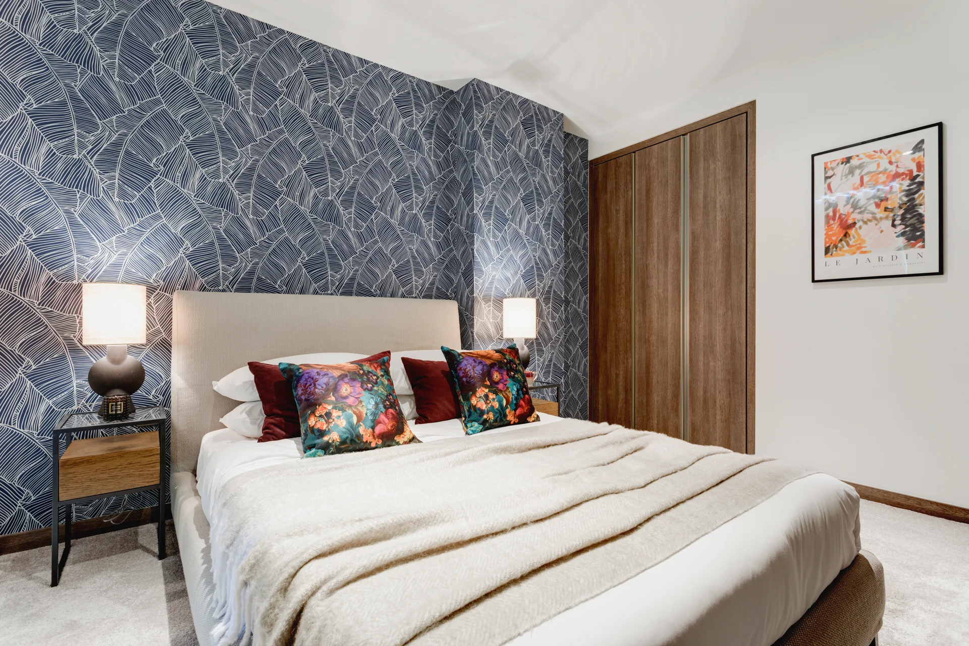 Cozy bedroom featuring a patterned blue wall, a bed with decorative pillows, and bedside lamps.