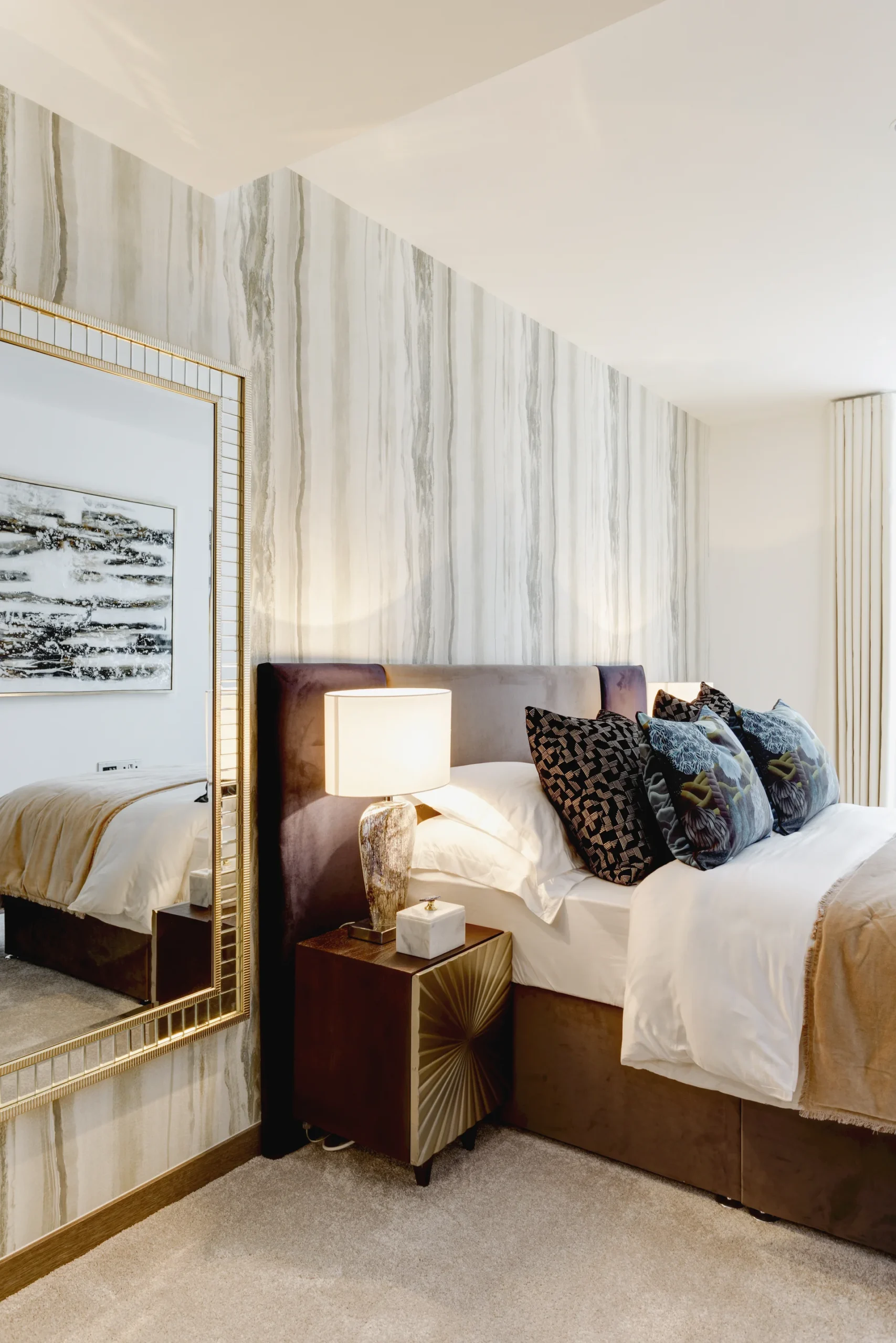 Luxury bedroom featuring a large mirror, plush bedding, and decorative pillows against a sleek striped wall.