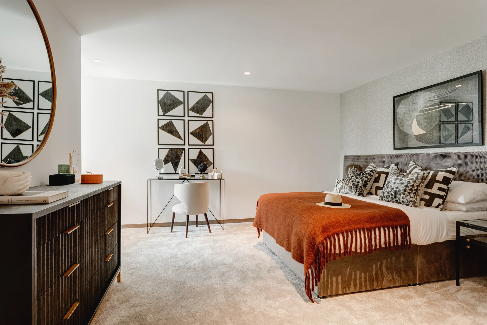 Modern bedroom featuring a bed with a rust-colored throw, decorative pillows, a stylish dresser, and a desk.