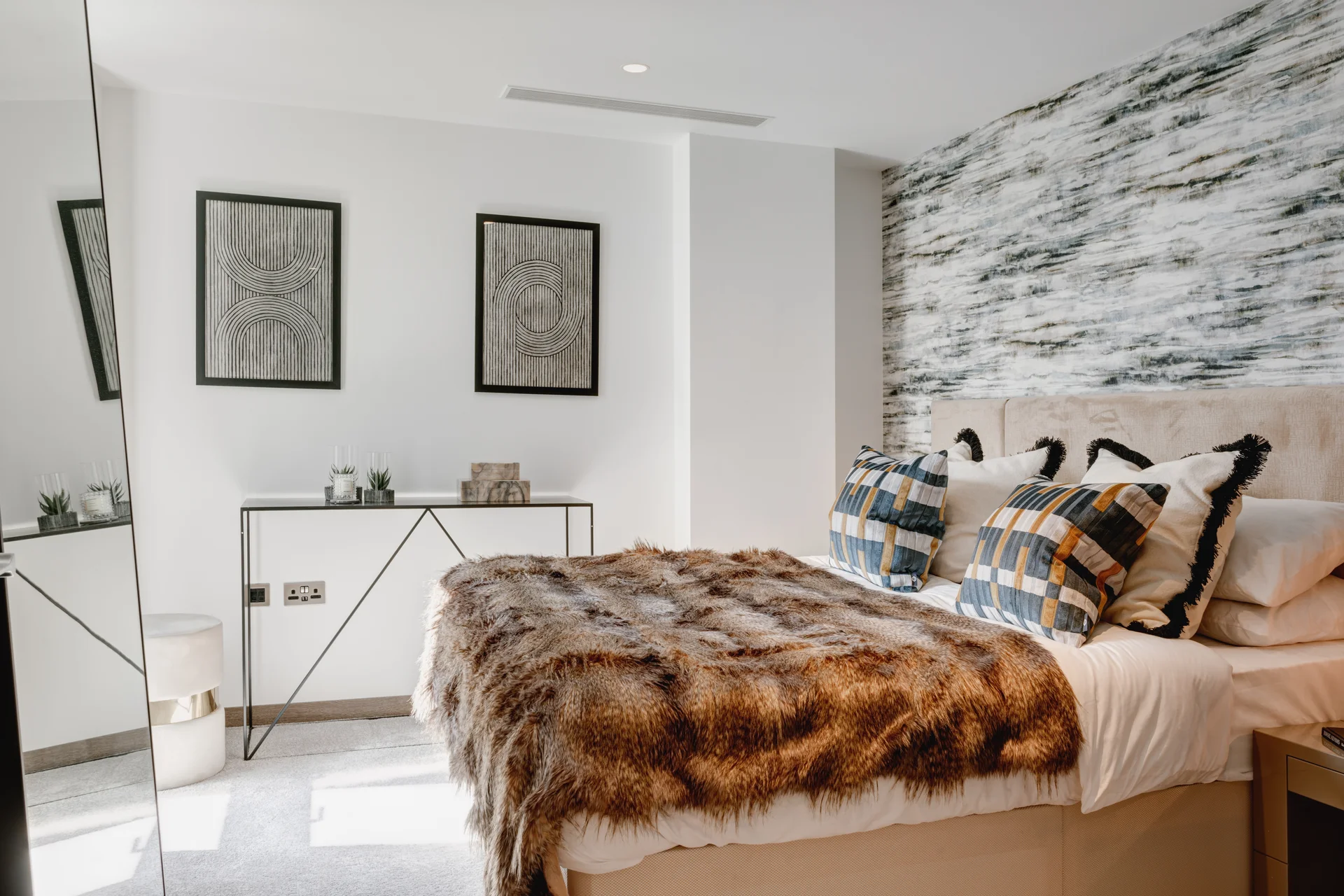 Modern bedroom featuring a cozy bed with a fur throw, decorative pillows, and stylish wall art.