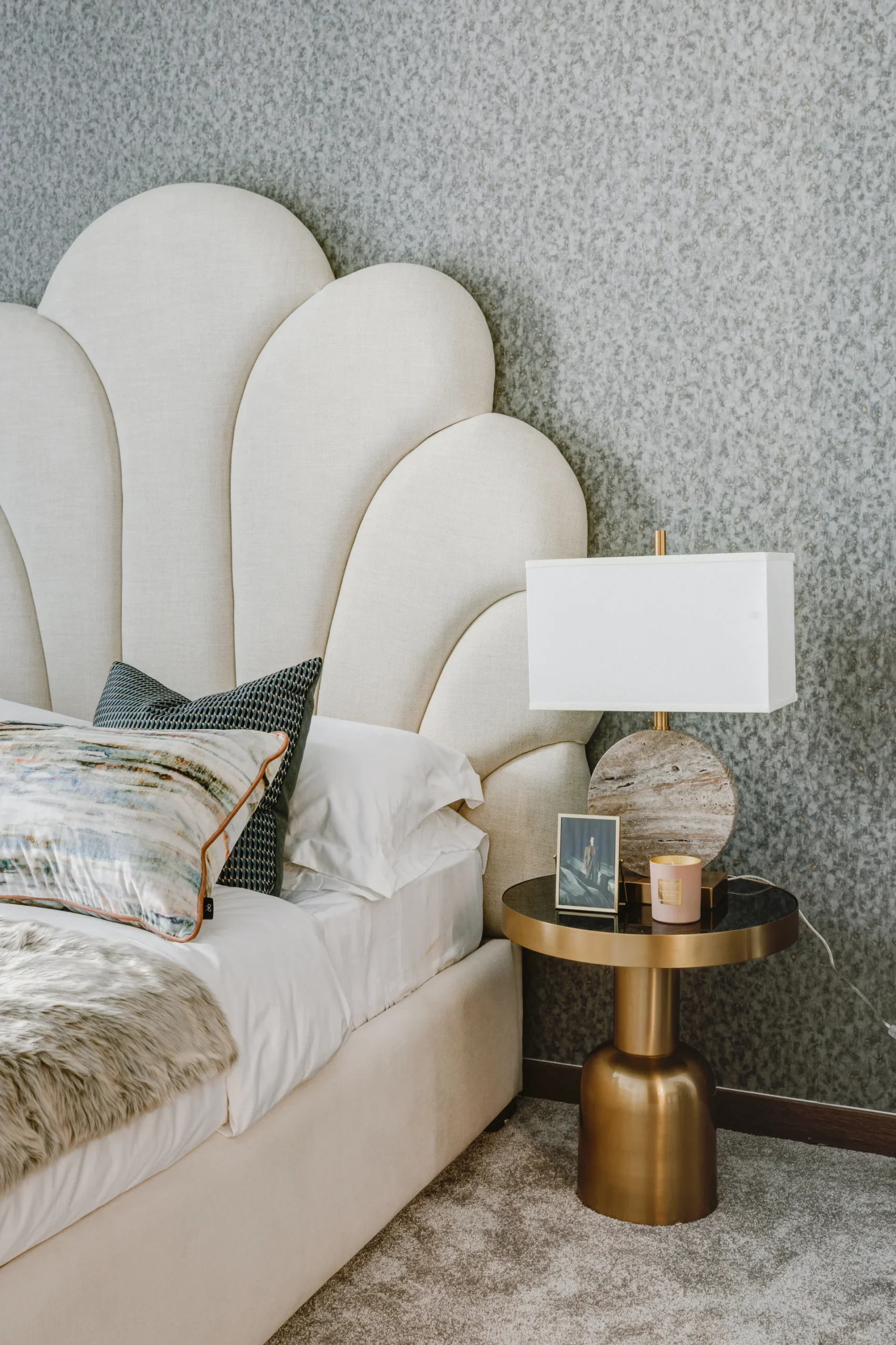 Stylish bedroom featuring a scalloped headboard, a cozy bed, and a modern lamp on a gold side table.