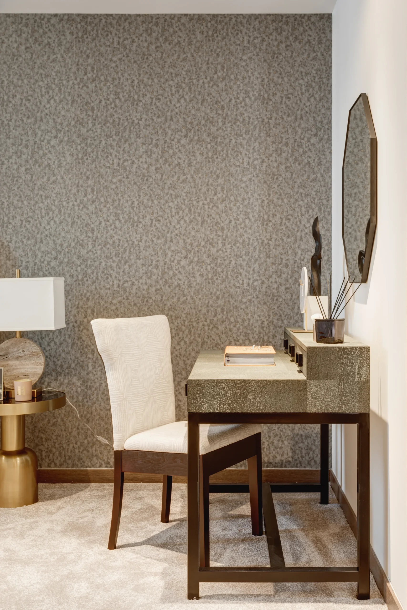 Modern desk with a chair, lamp, and decorative mirror against a textured wall in a stylish interior setting.