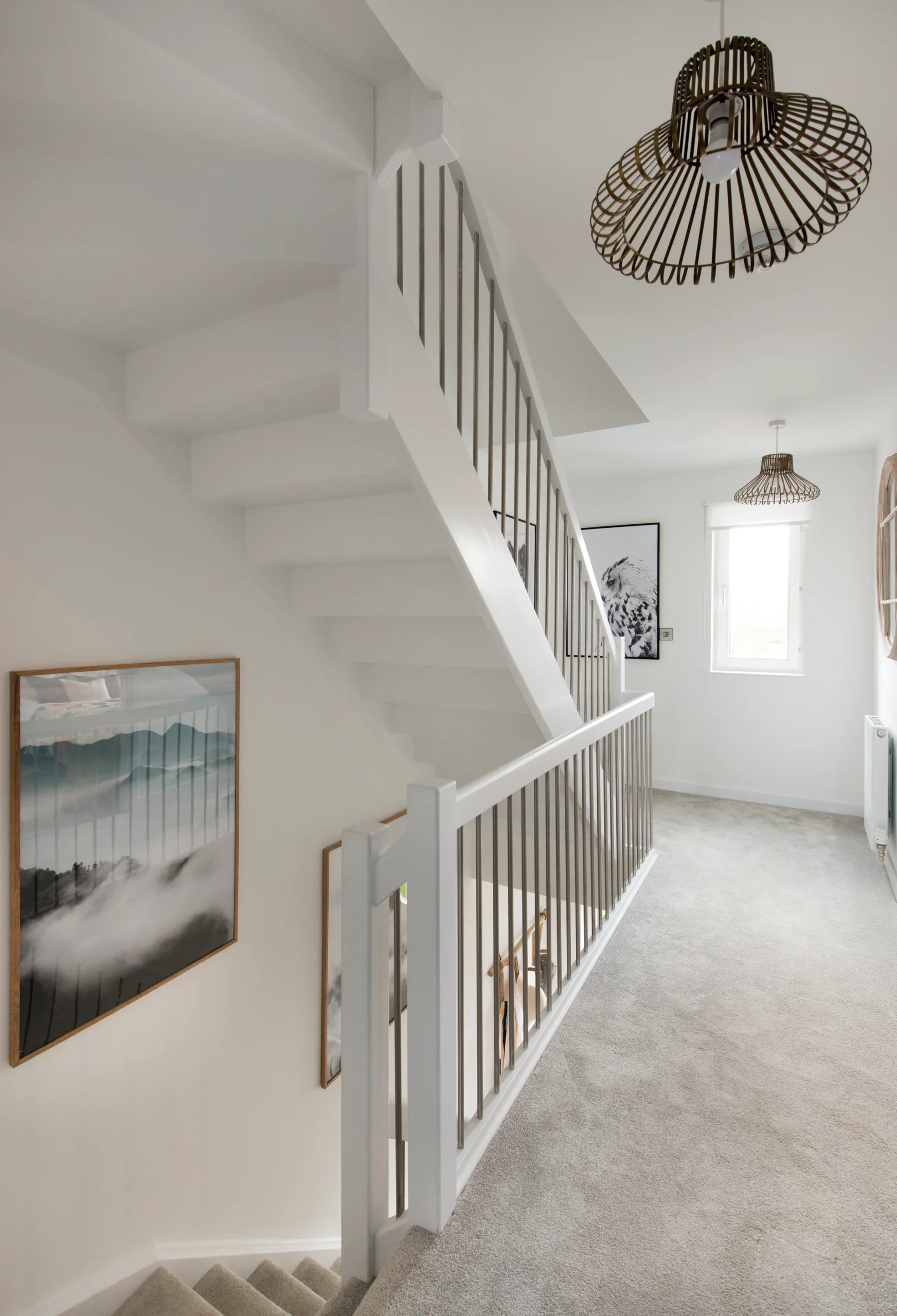 Light-filled staircase with wooden railing, decorative light fixtures, and framed artwork on the walls.