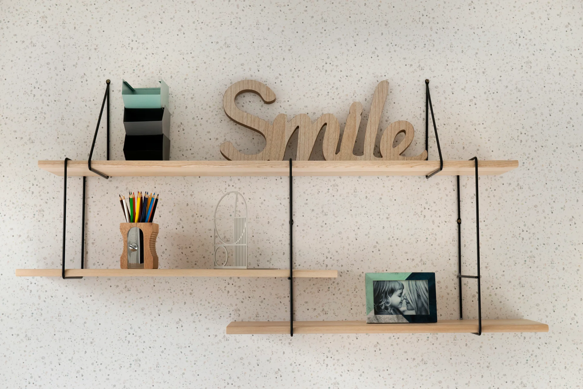 Wooden shelves displaying a "Smile" sign, colored pencils, and framed photos against a speckled wall.