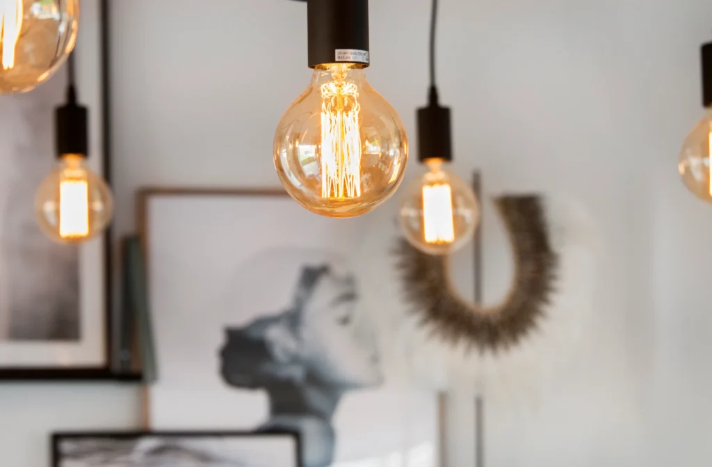 Hanging Edison-style light bulbs with a blurred background featuring a woman’s portrait and decorative art.