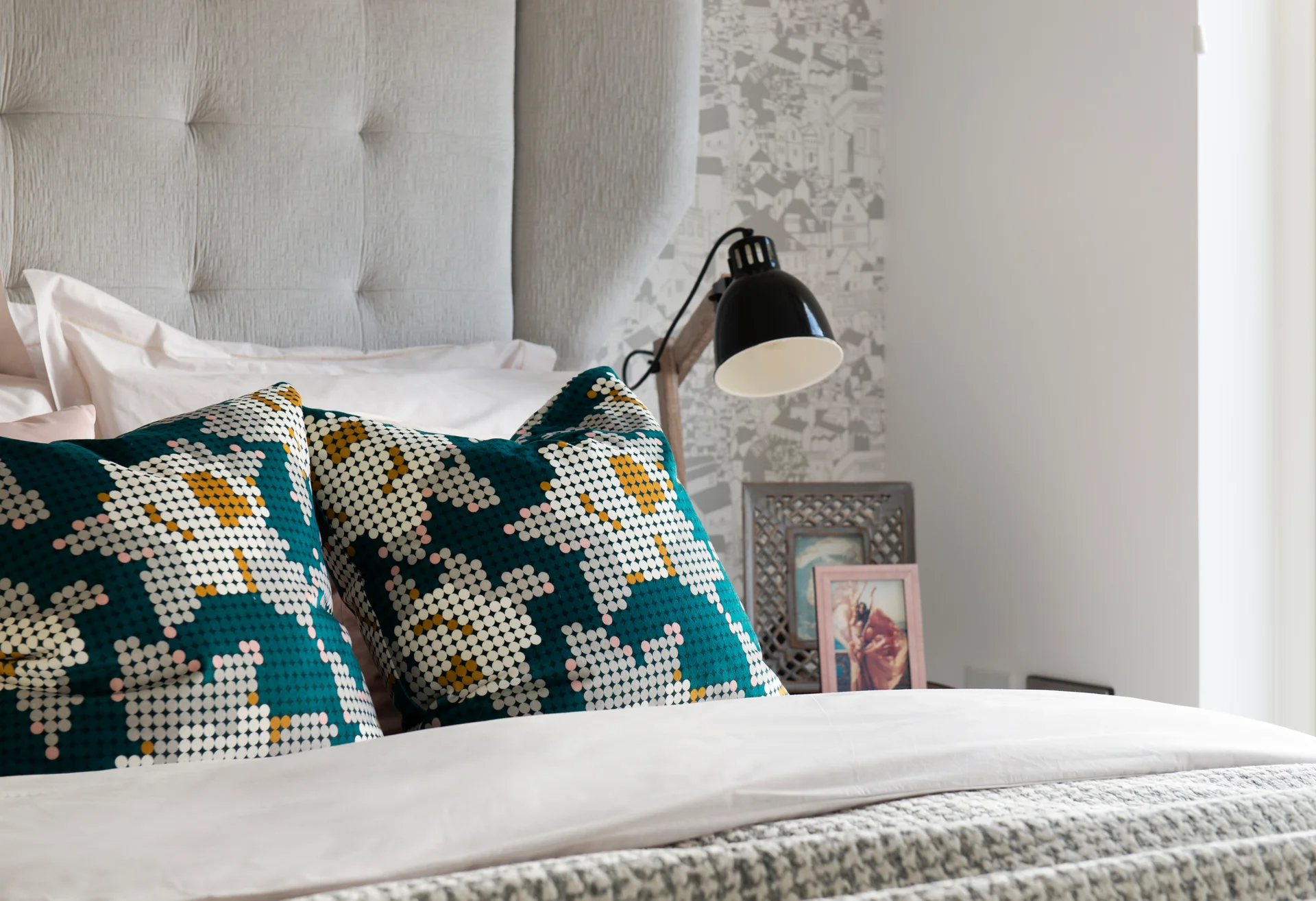 Cozy bedroom scene featuring decorative pillows, a bedside lamp, and a framed photo on a nightstand.