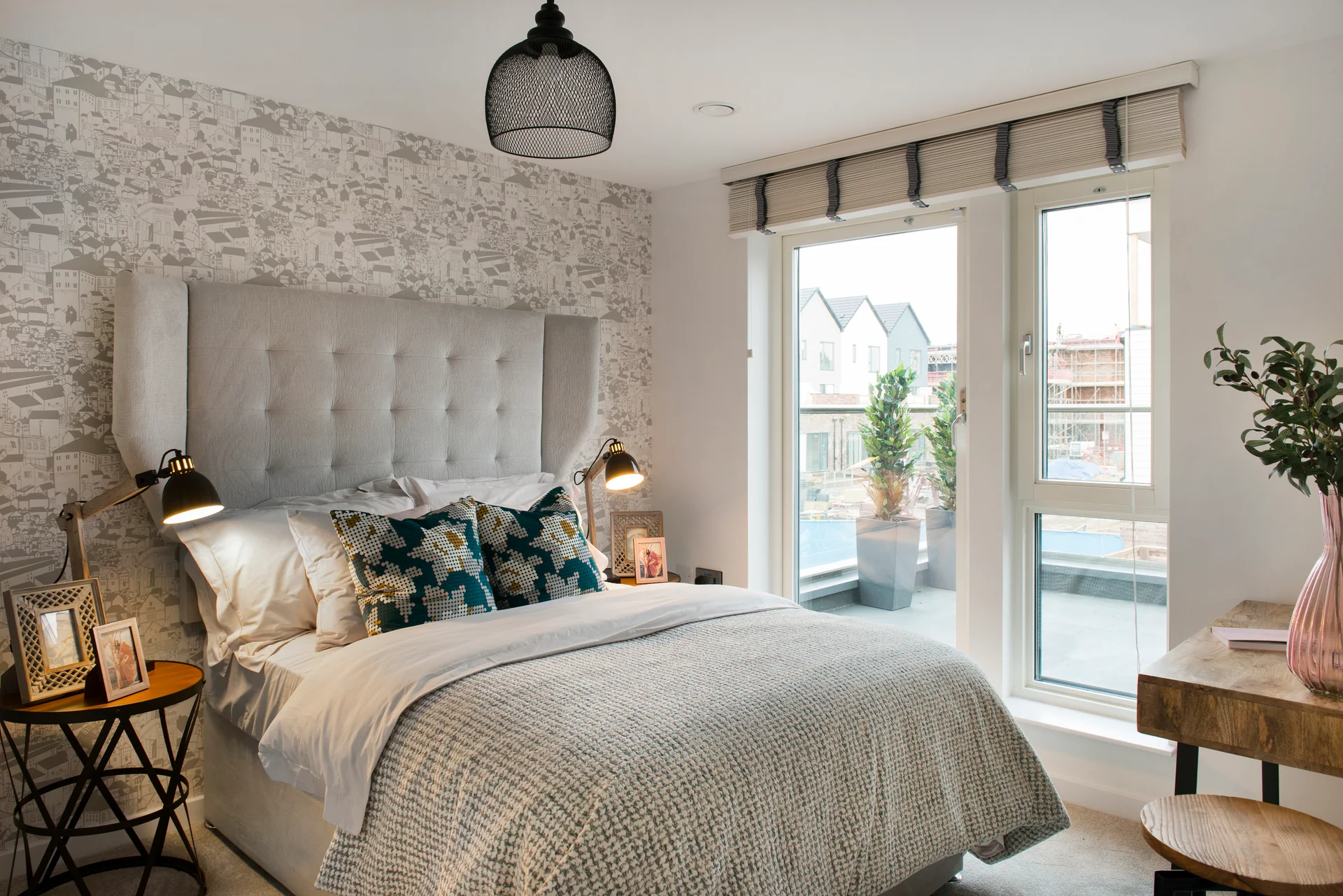 Stylish bedroom with a tufted headboard, floral pillows, and large windows overlooking an outdoor space.