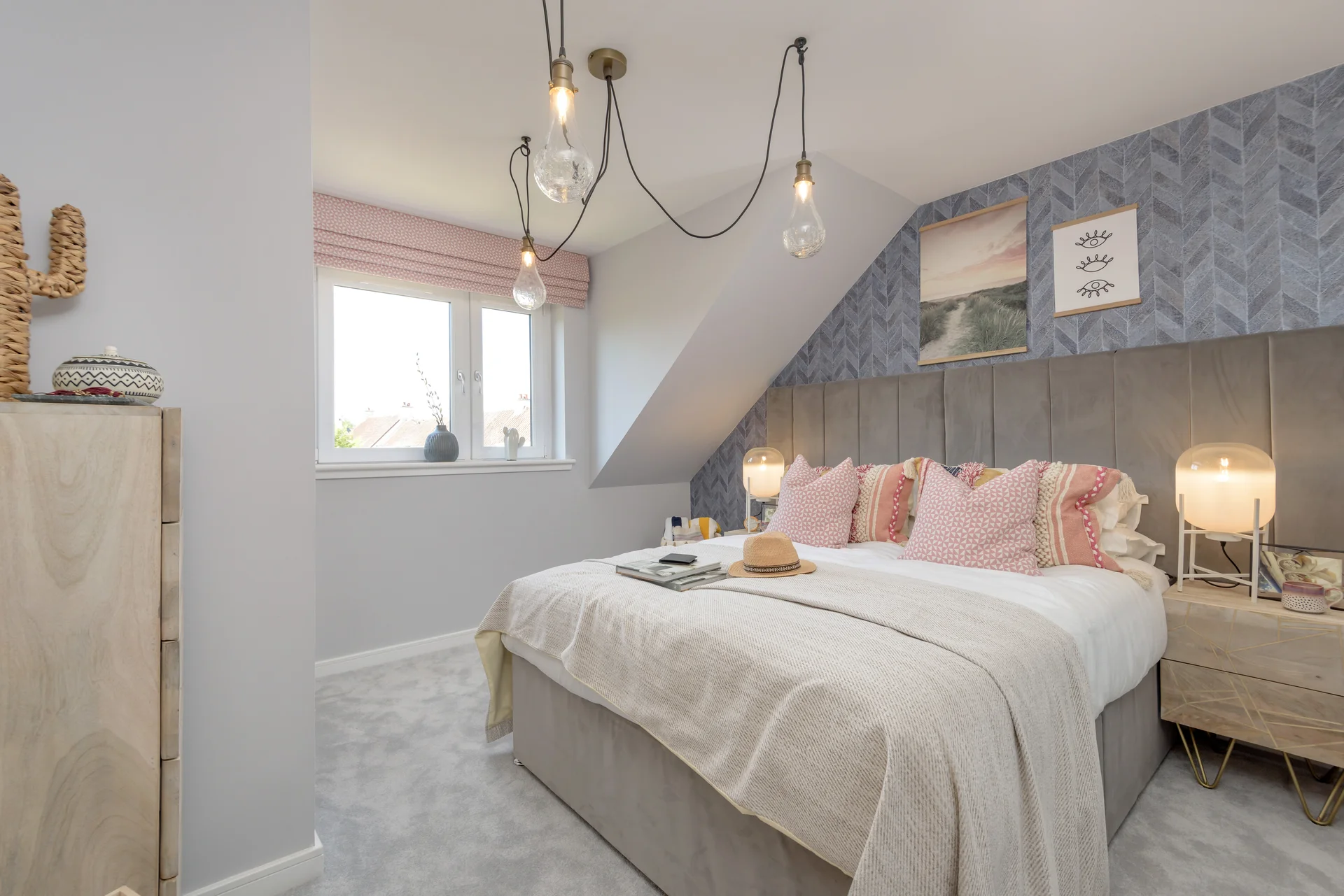 Modern bedroom with a grey upholstered bed, pink pillows, decorative lighting, and light grey carpet.