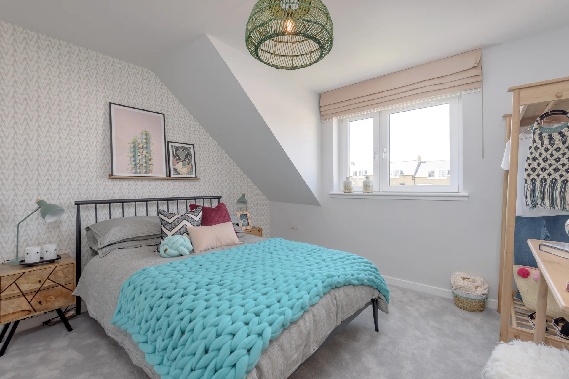 Cozy bedroom with a grey bed, turquoise blanket, patterned wall, and a pendant light, featuring a window with natural light.