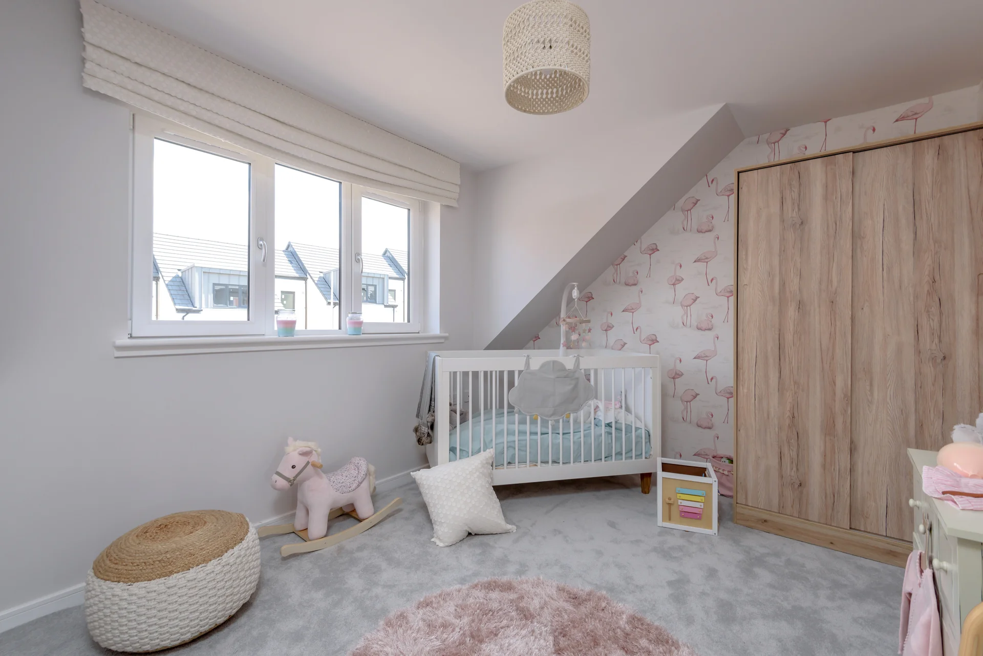 Bright nursery featuring a crib, soft rug, toy storage, and floral wallpaper under a slanted ceiling.