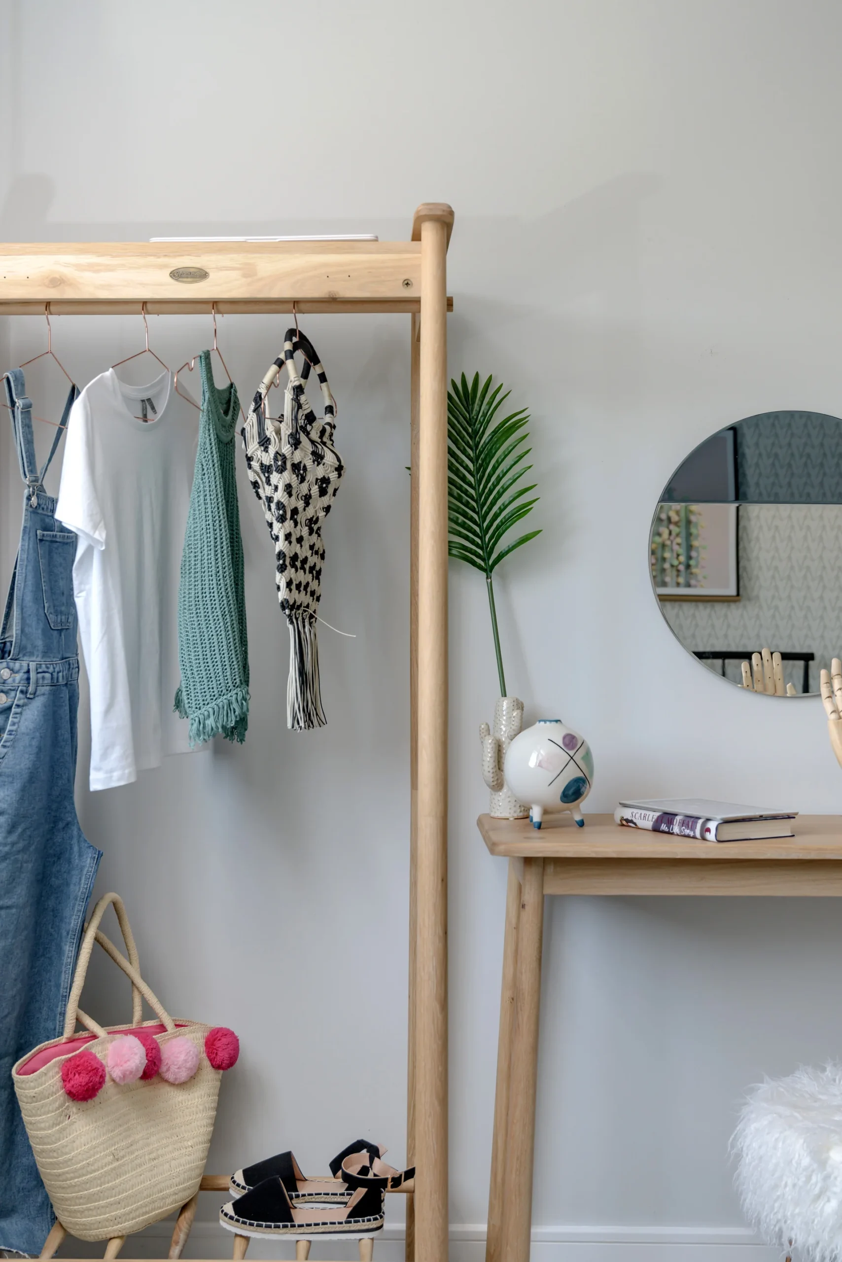 A wooden clothing rack displays outfits beside a small round mirror and a table with decorative items.
