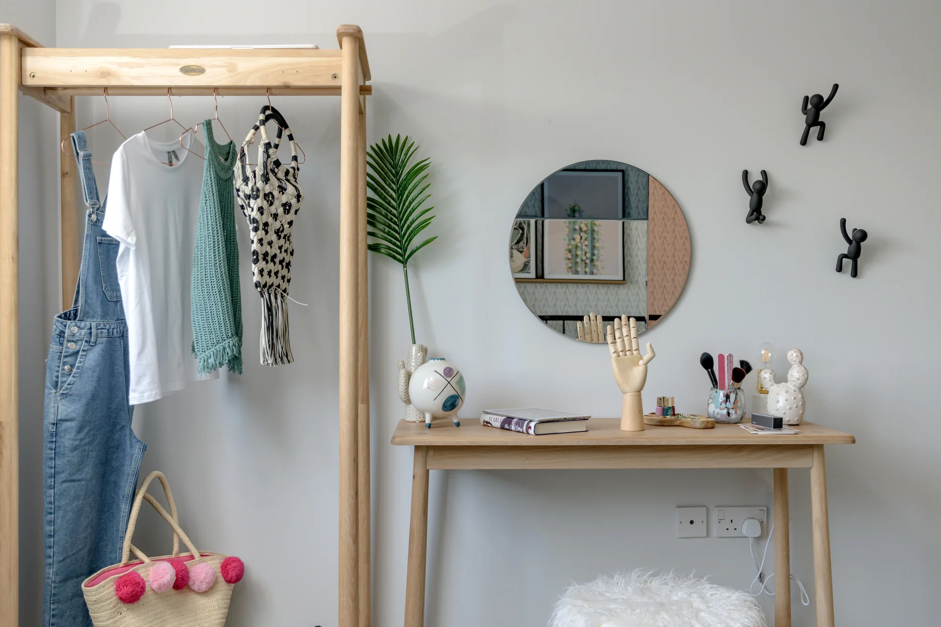 Clothing on a rack beside a small table with decor items, a mirror, and wall art in a modern room setting.