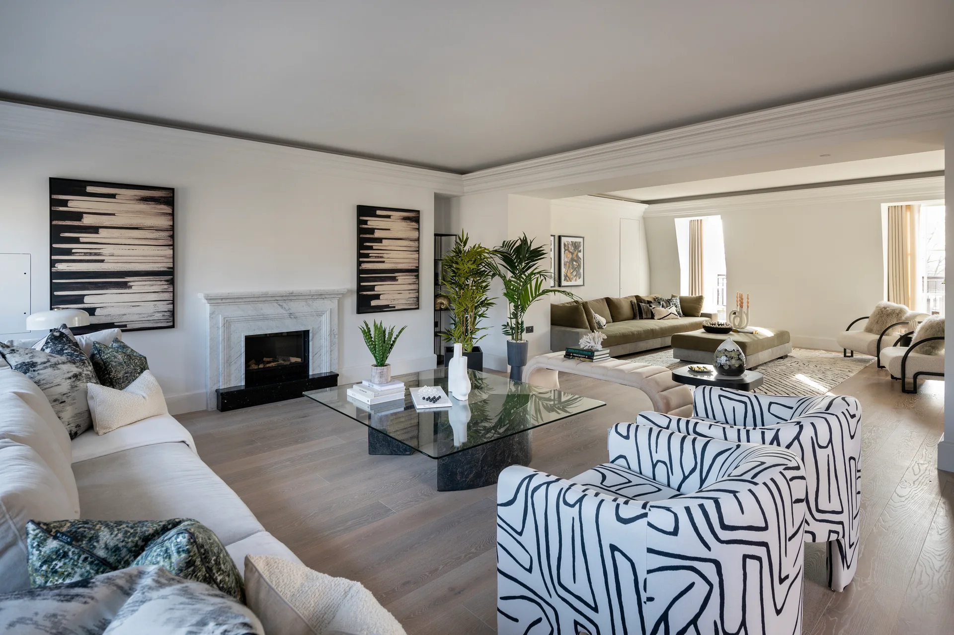 Spacious living room with modern furniture, abstract art, and a fireplace, featuring plants and large windows for natural