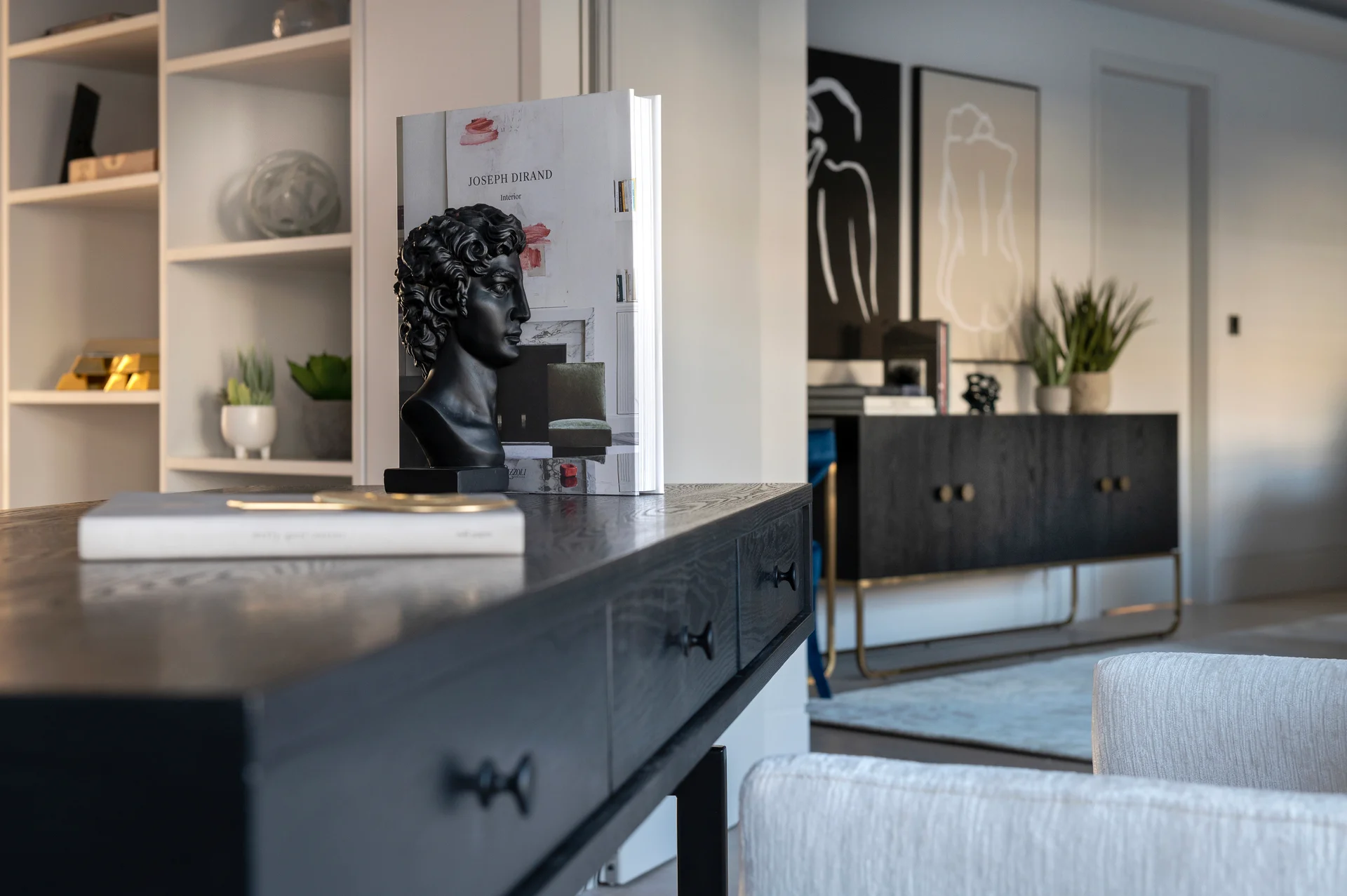 Modern living space featuring a dark cabinet, decorative books, a sculpture, and abstract wall art.