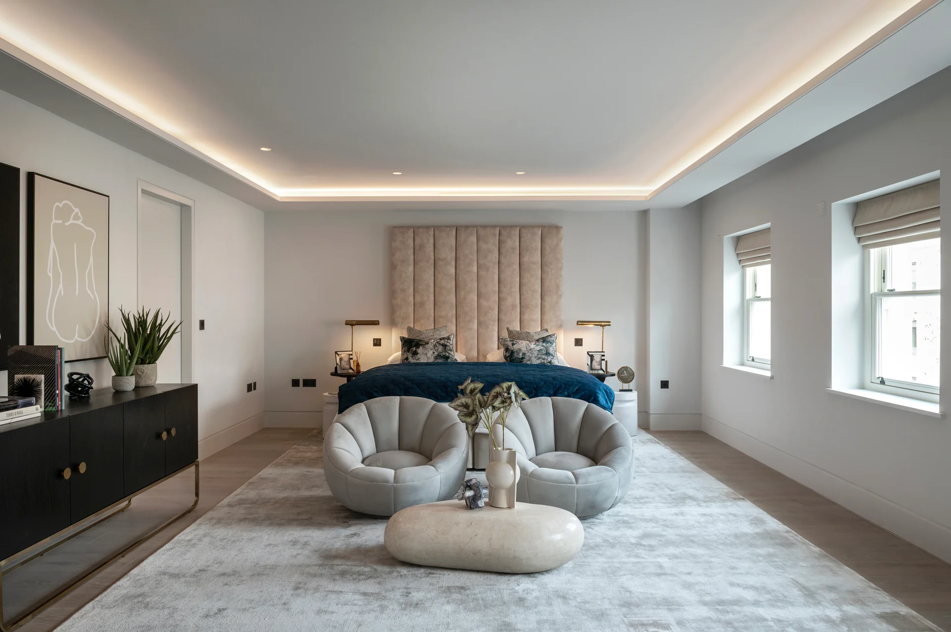 Spacious bedroom featuring a blue bed, organic-shaped seating, and soft lighting for a modern aesthetic.