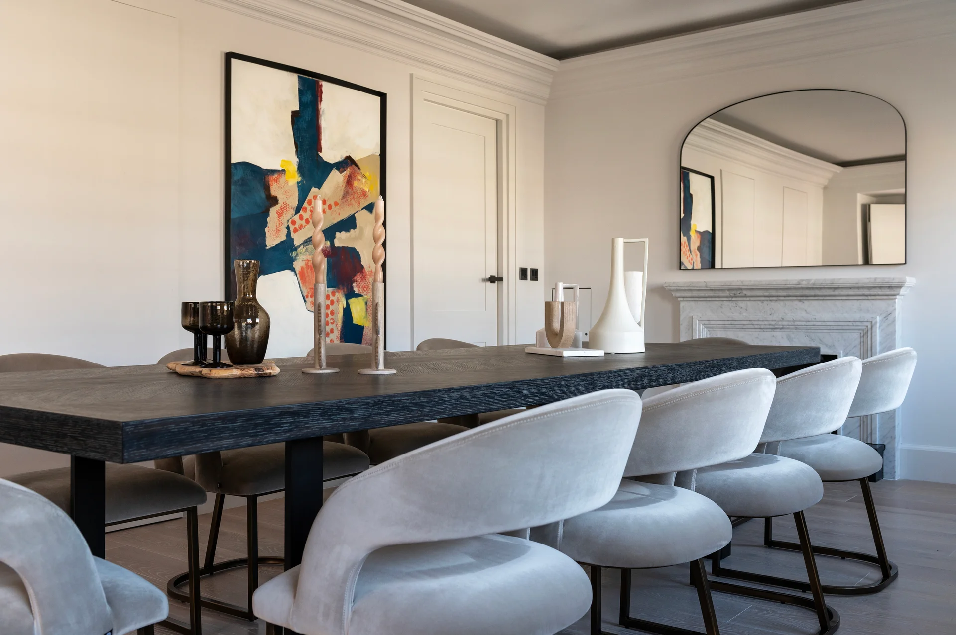 Modern dining room featuring a large table, plush chairs, colorful artwork, and a stylish mirror.