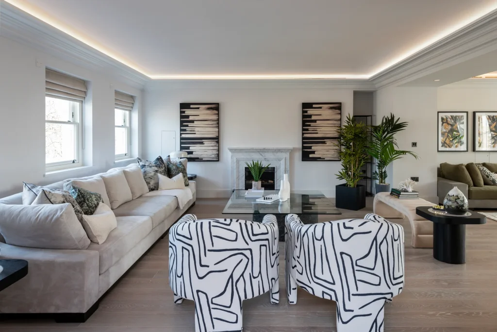 Modern living room featuring a light-colored sofa, patterned chairs, plants, and contemporary artwork on the walls.