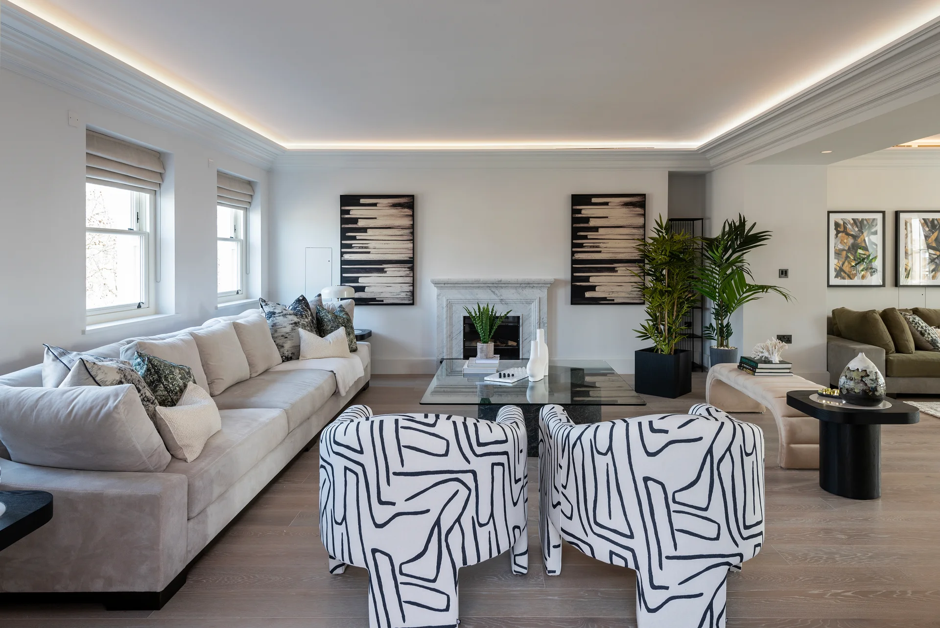 Modern living room featuring a light-colored sofa, patterned chairs, plants, and contemporary artwork on the walls.