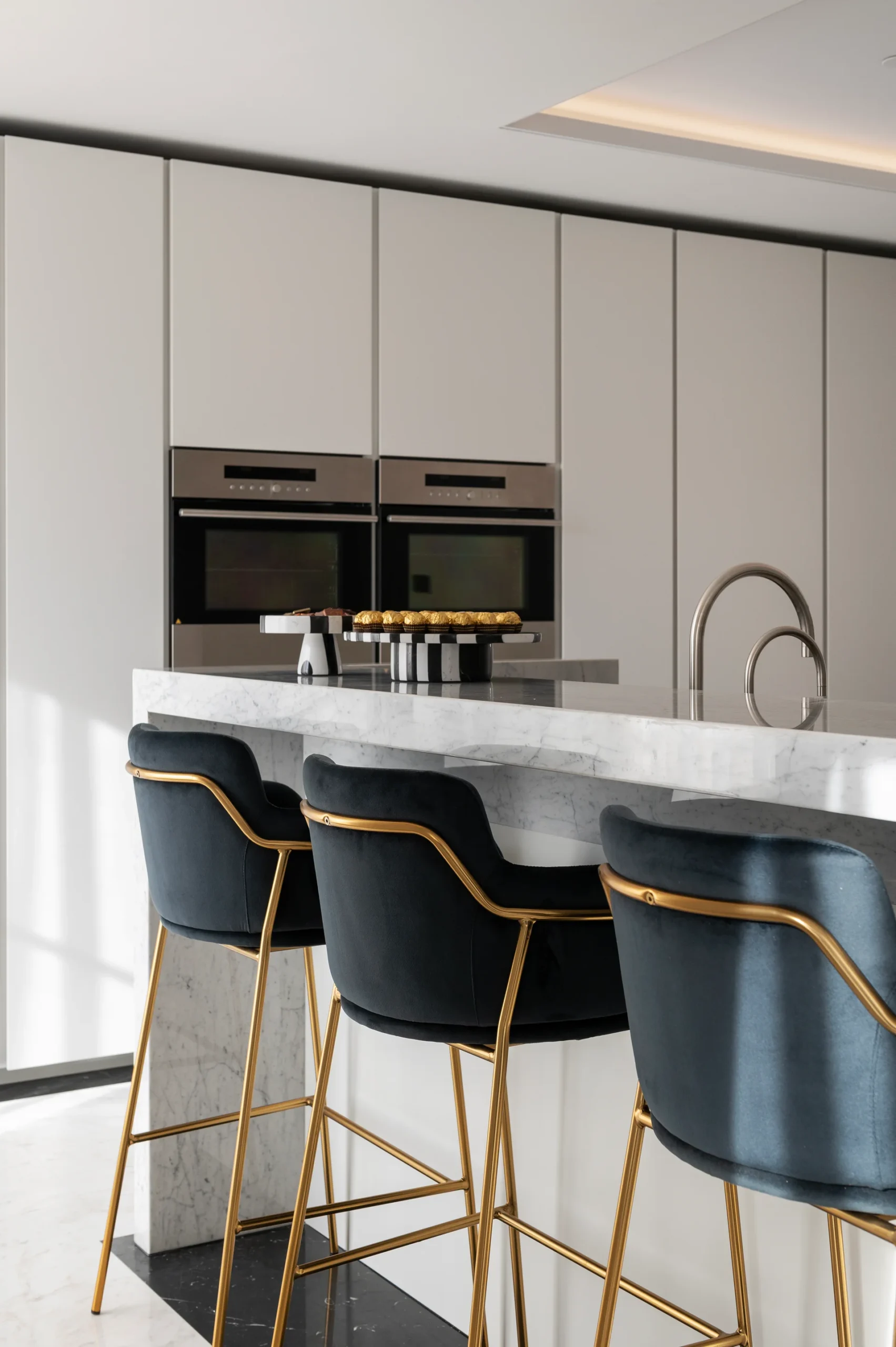 Modern kitchen featuring sleek cabinetry, stainless steel appliances, and stylish black bar stools with gold accents.