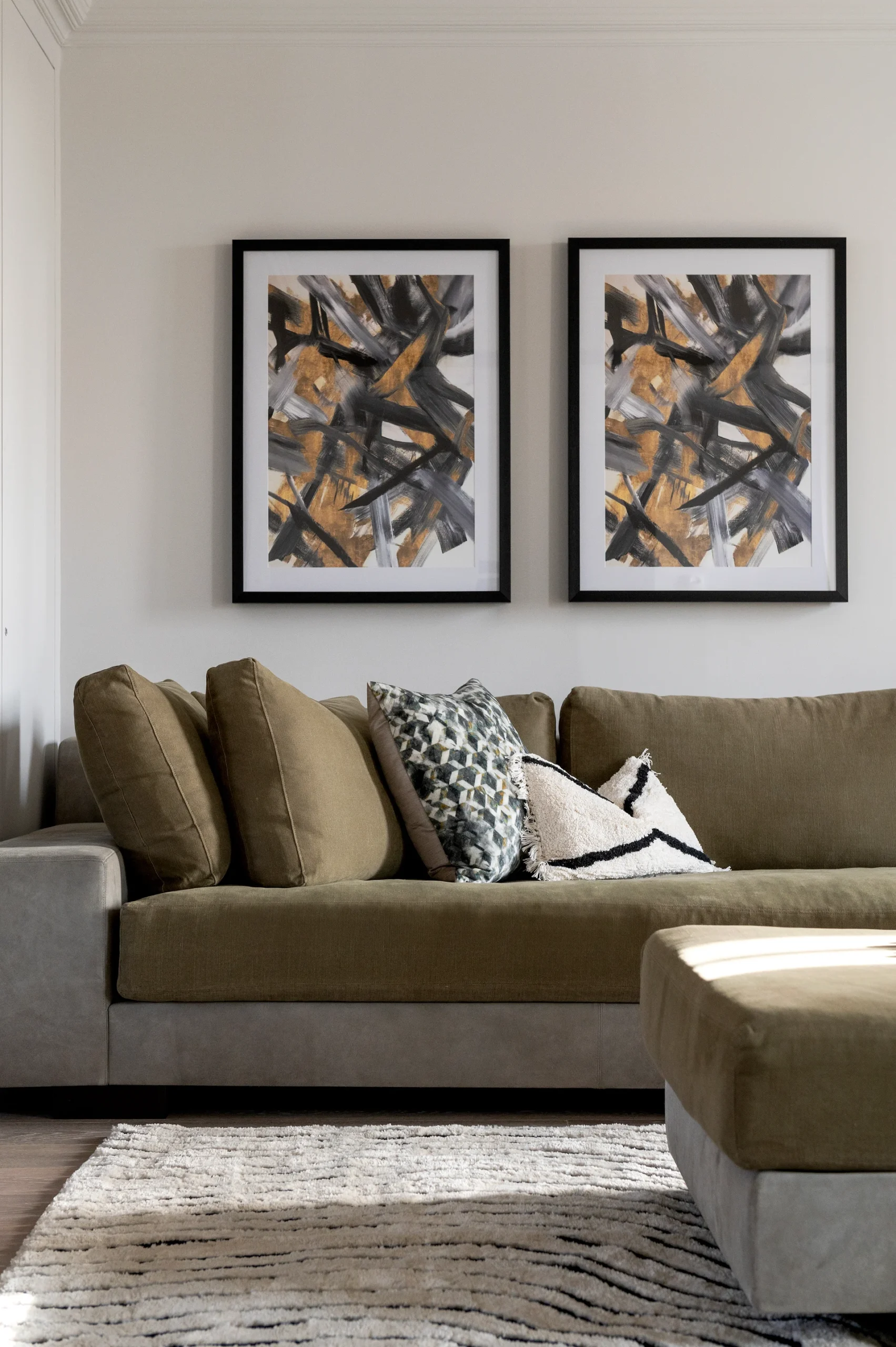 Cozy living room featuring a large olive green sectional sofa with decorative pillows and two abstract framed artworks.