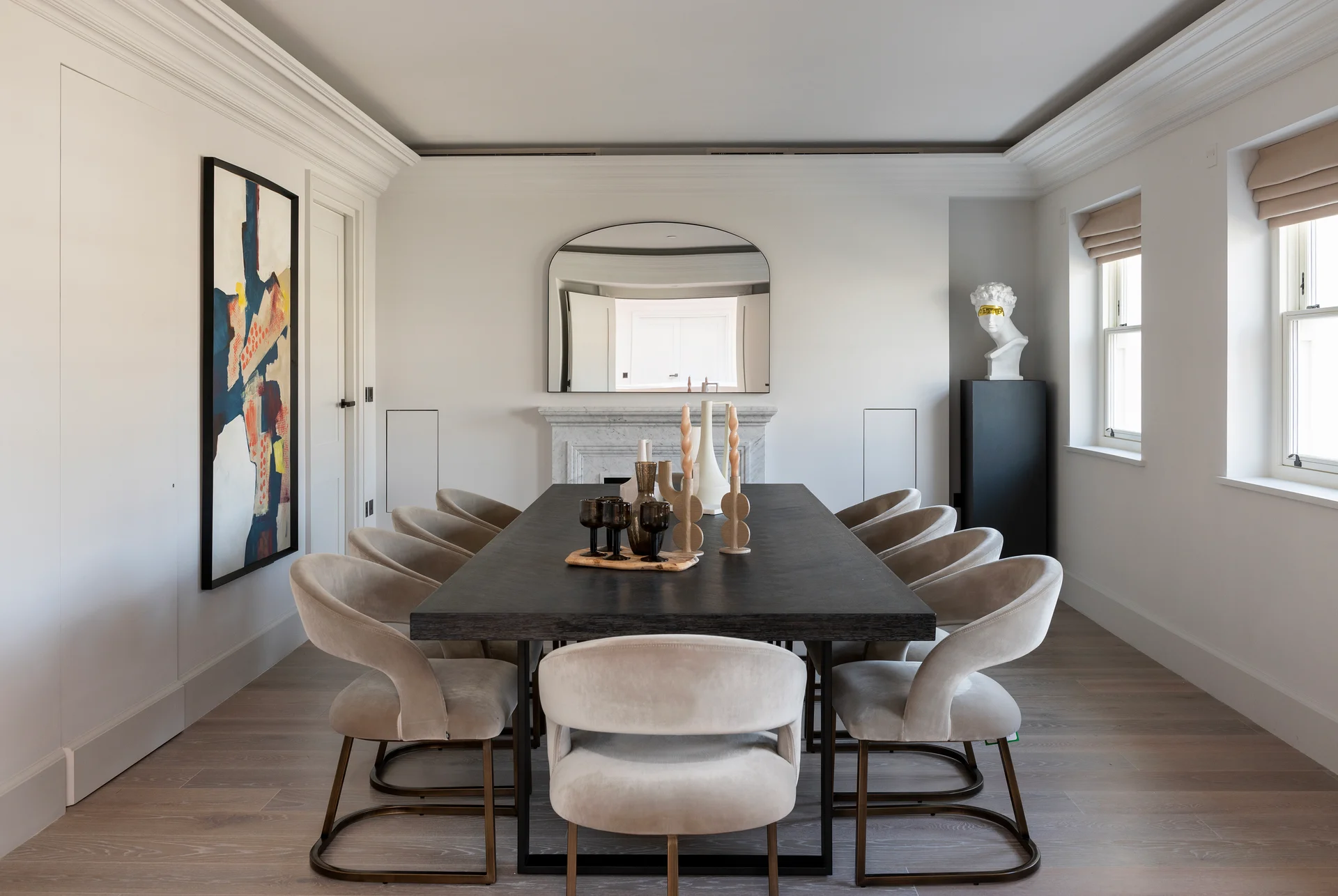 Modern dining room with a large table, upholstered chairs, abstract art, and a decorative mirror on the wall.