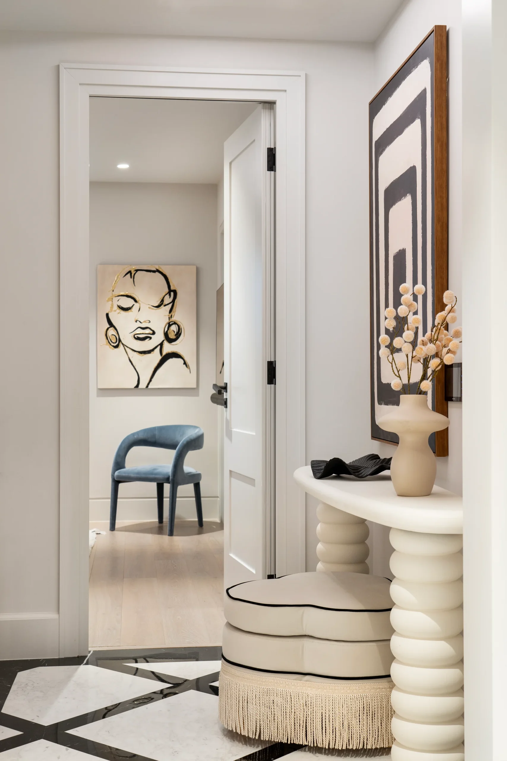 A stylish hallway featuring modern art, a round table with a vase, and a blue chair in the background.