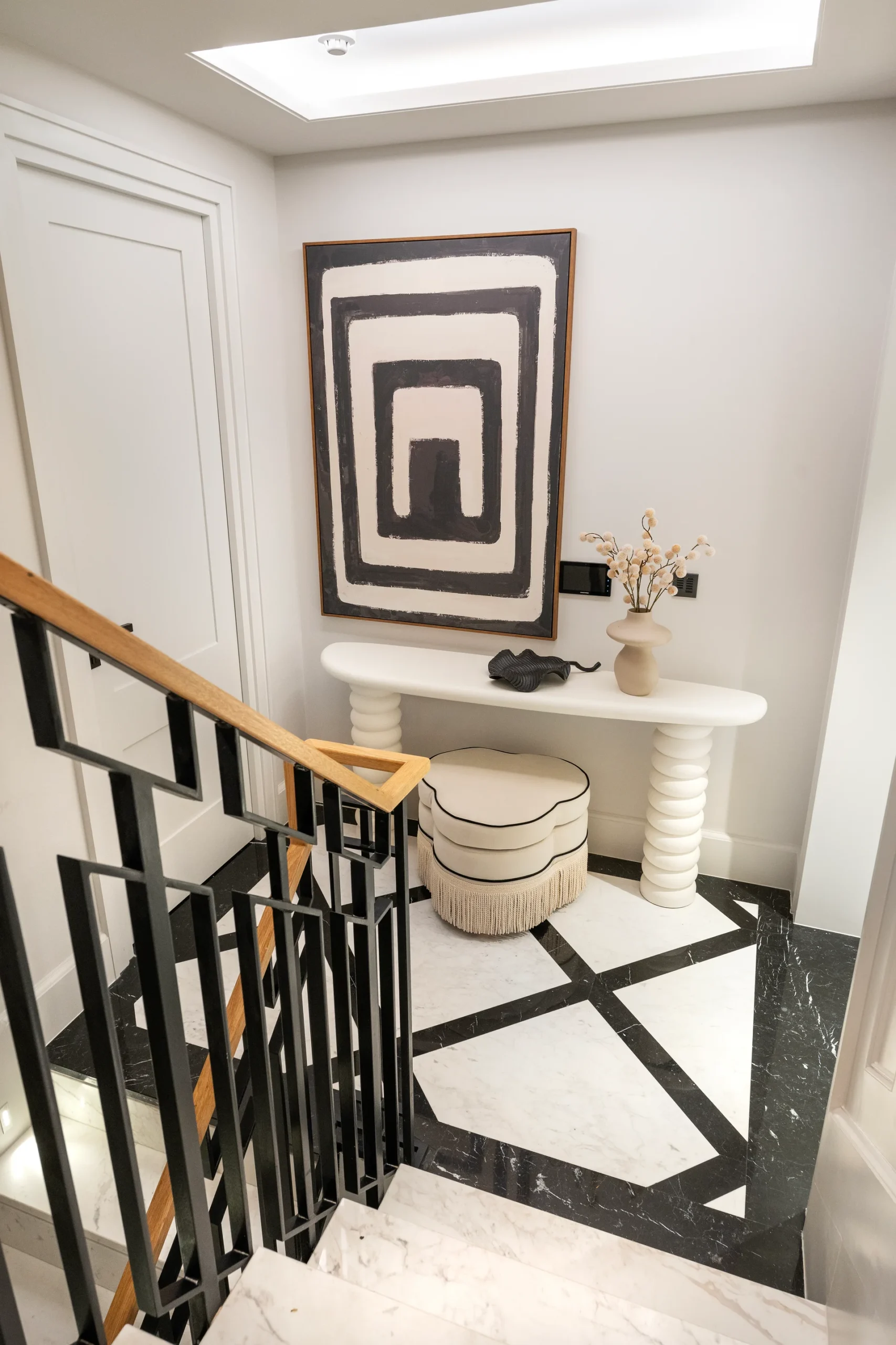 Modern staircase with black railing, decorative console table, and abstract artwork on the wall in a stylish entryway.