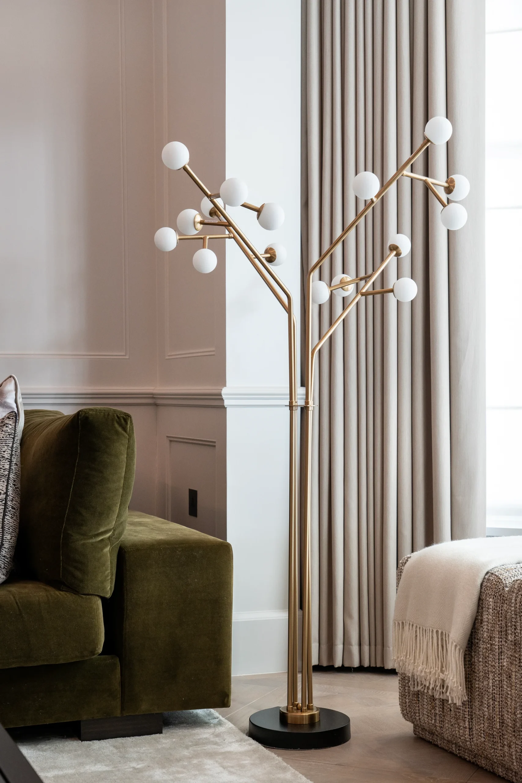 A modern floor lamp with a gold frame and white globe shades, situated near a green couch and curtains.