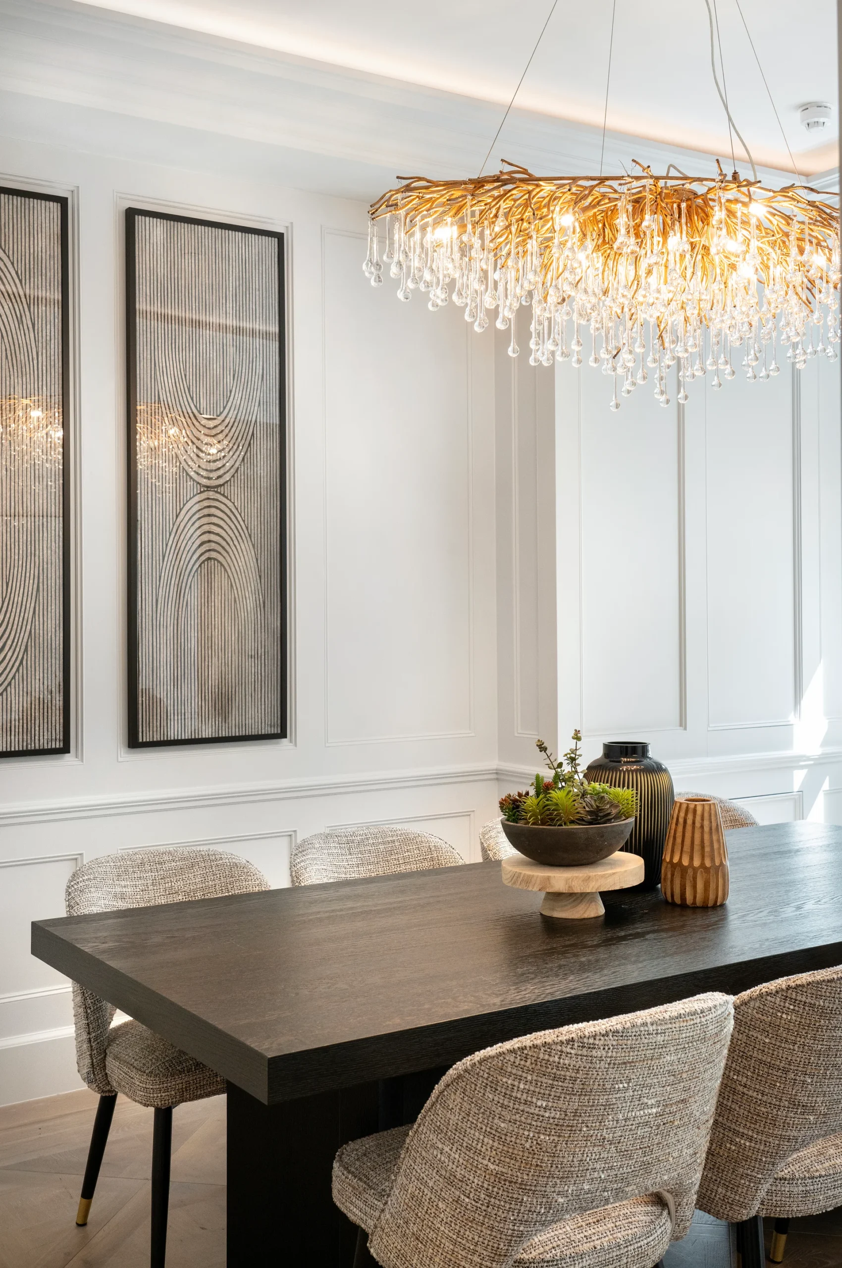 Modern dining area featuring a black table, woven chairs, and an elegant chandelier with decorative wall art.